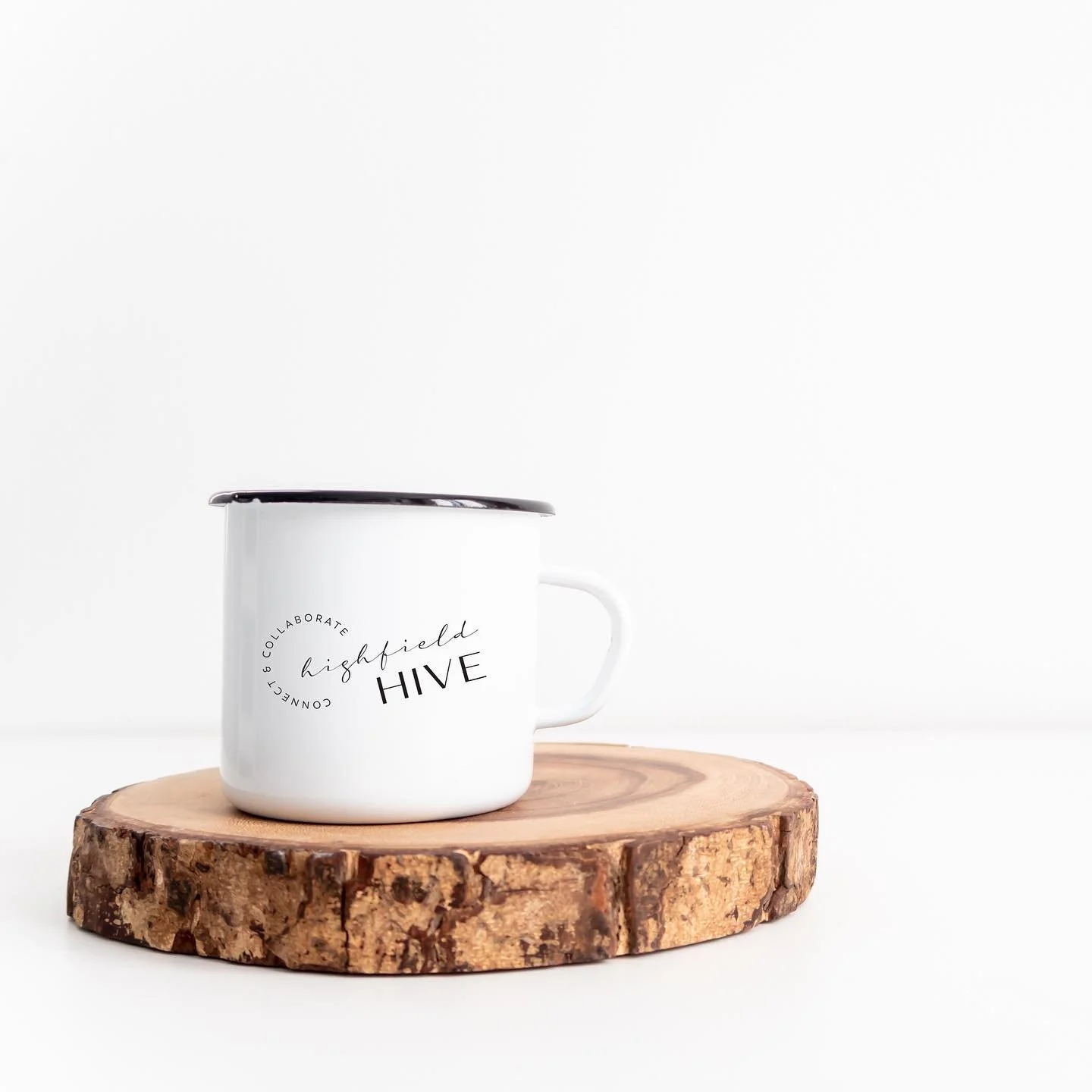 White enamel mug with 'Highfield Hive' logo on wooden slice against white background.