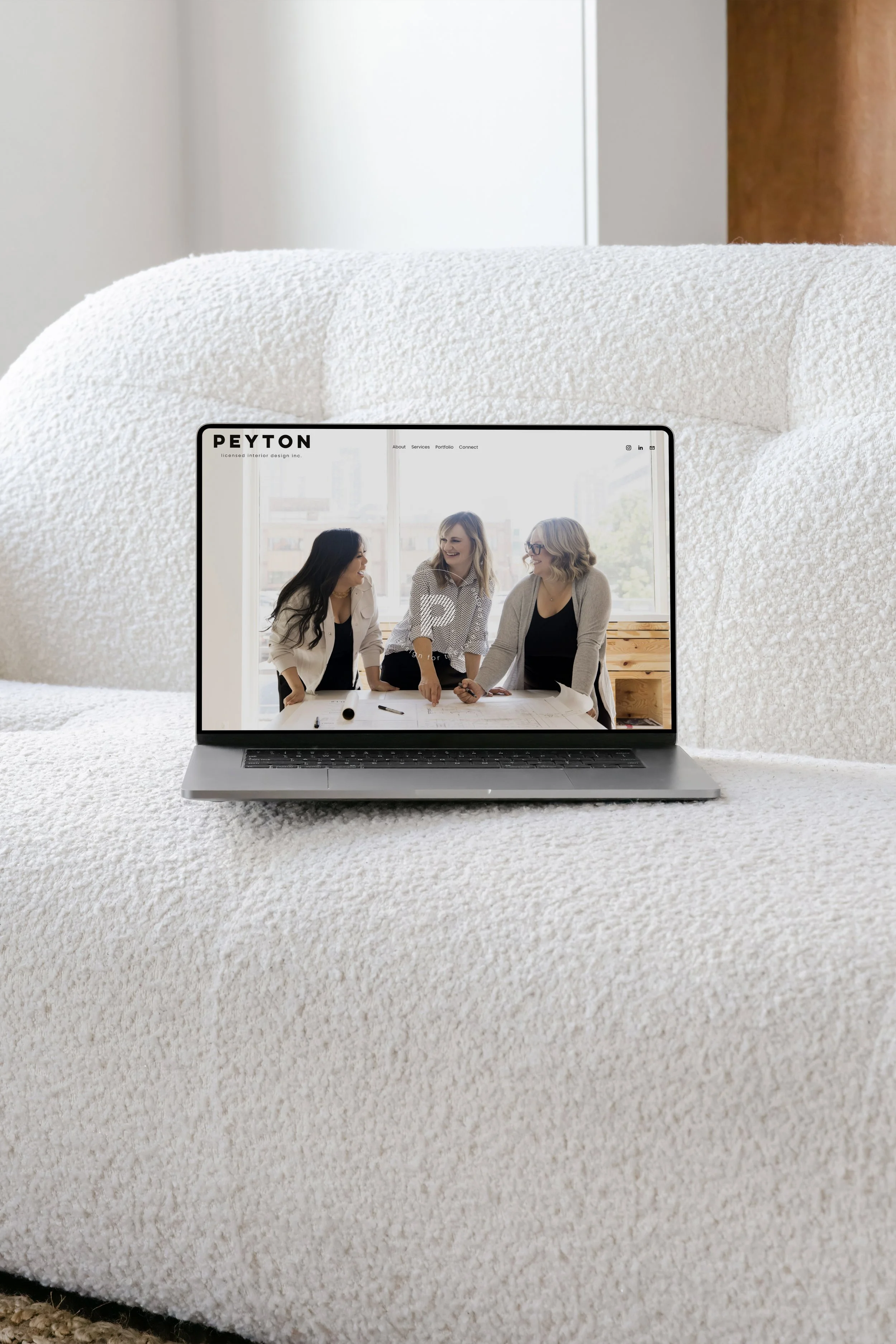 A laptop displaying a website on a fluffy white couch, with three people discussing plans on the screen.