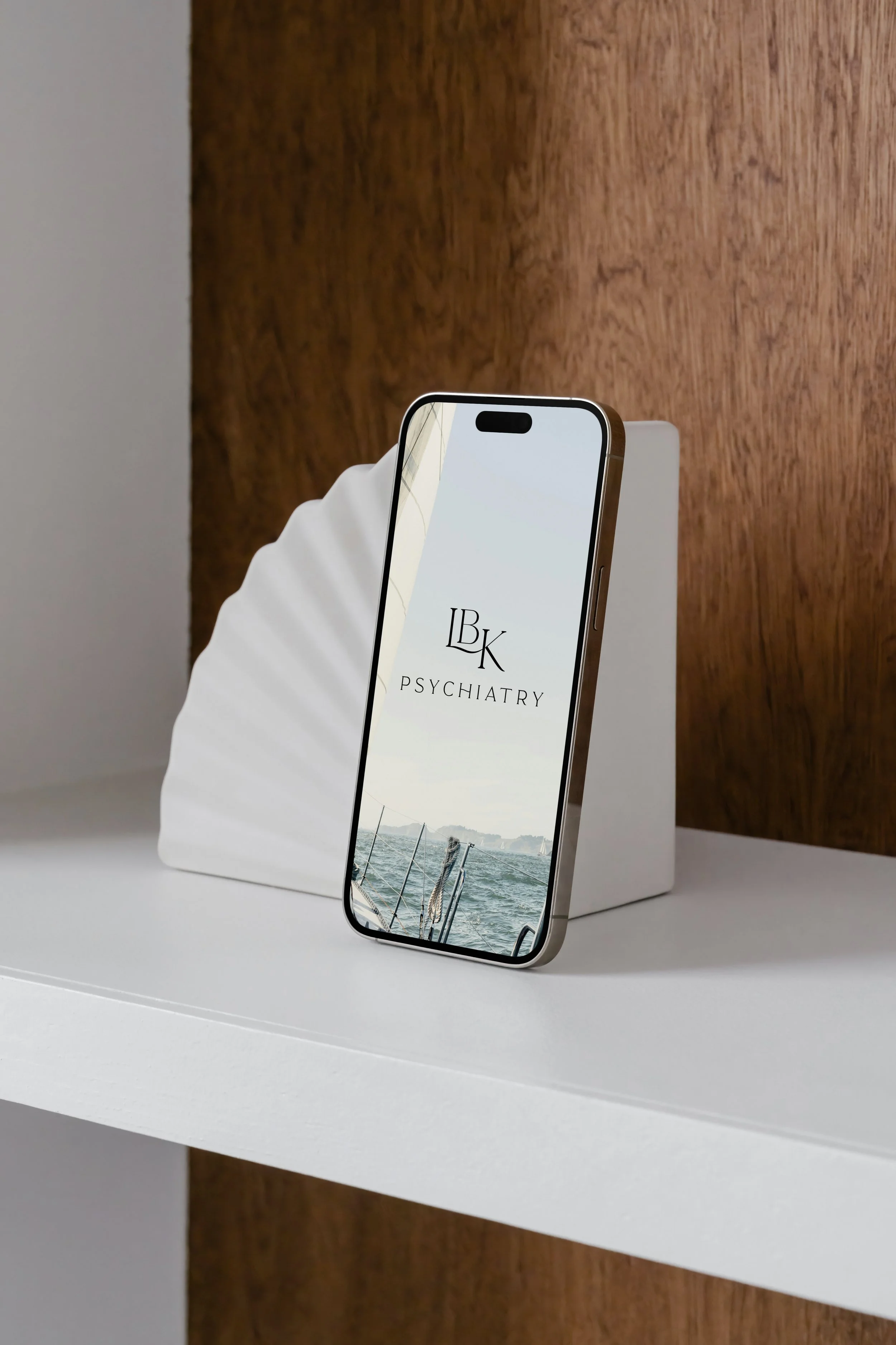Smartphone displaying "LBK Psychiatry" logo, propped on a white stand with a wooden background.