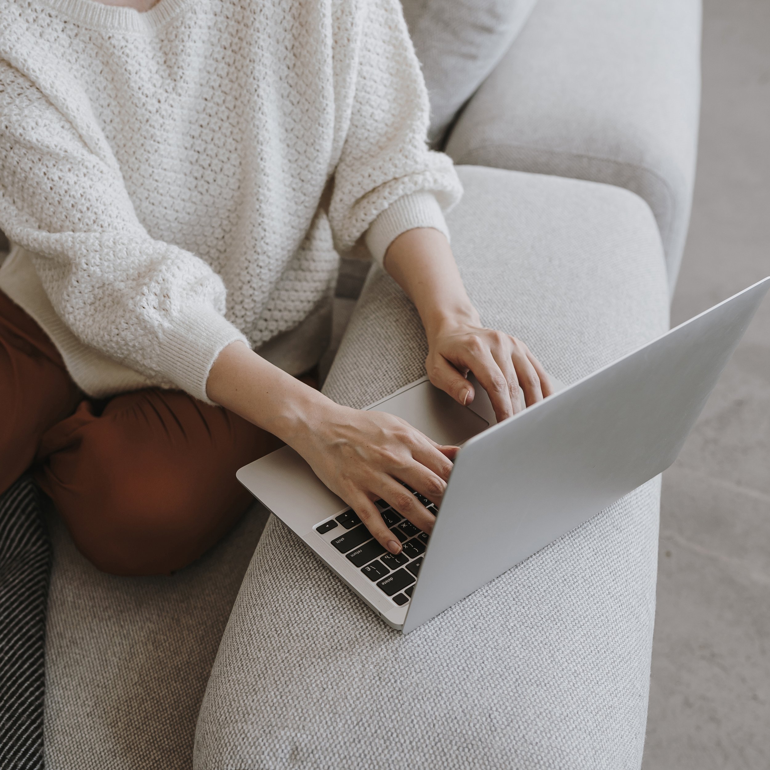 Person typing on a laptop while sitting on a sofa