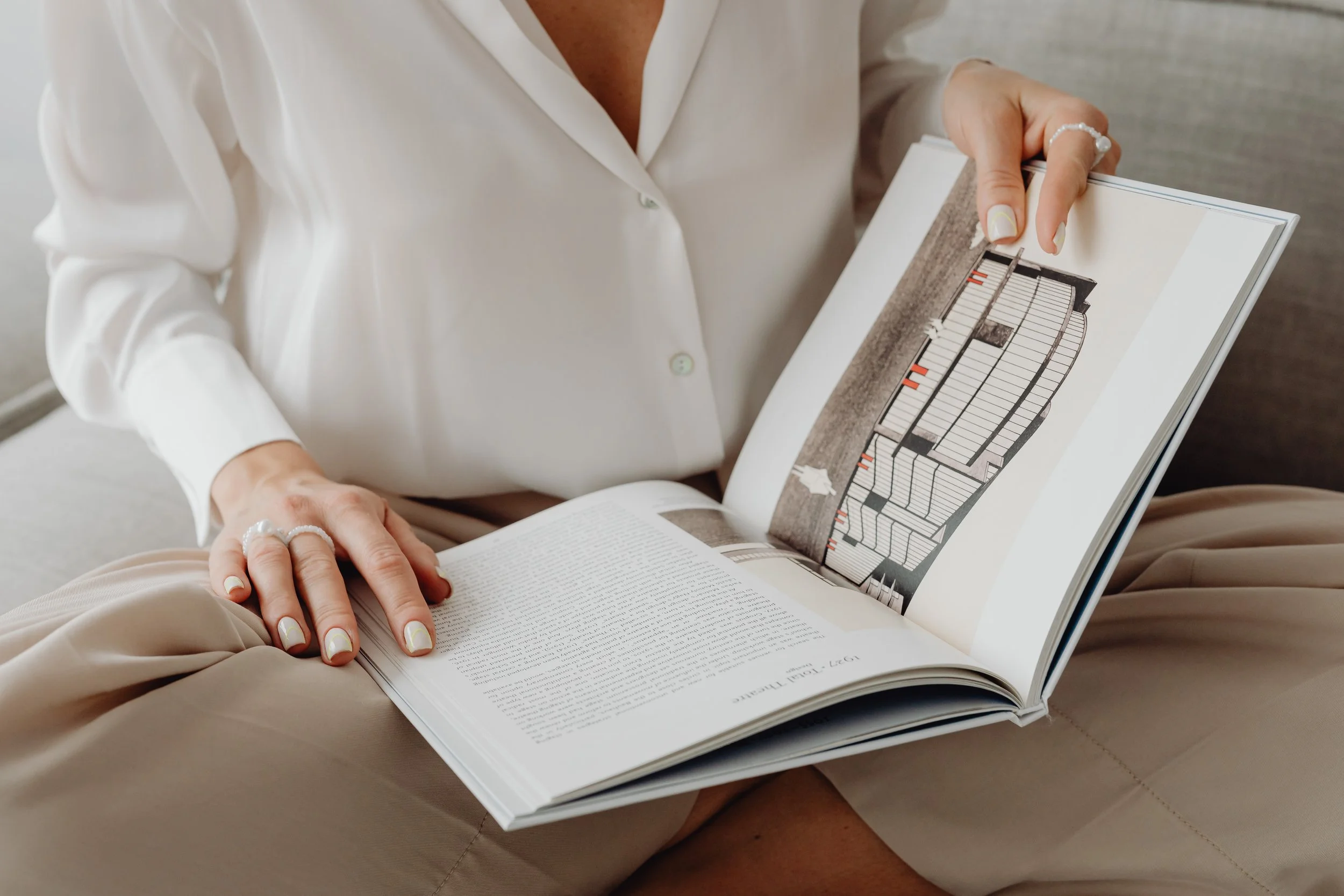 Person wearing a white blouse reading an open book with an architectural illustration.