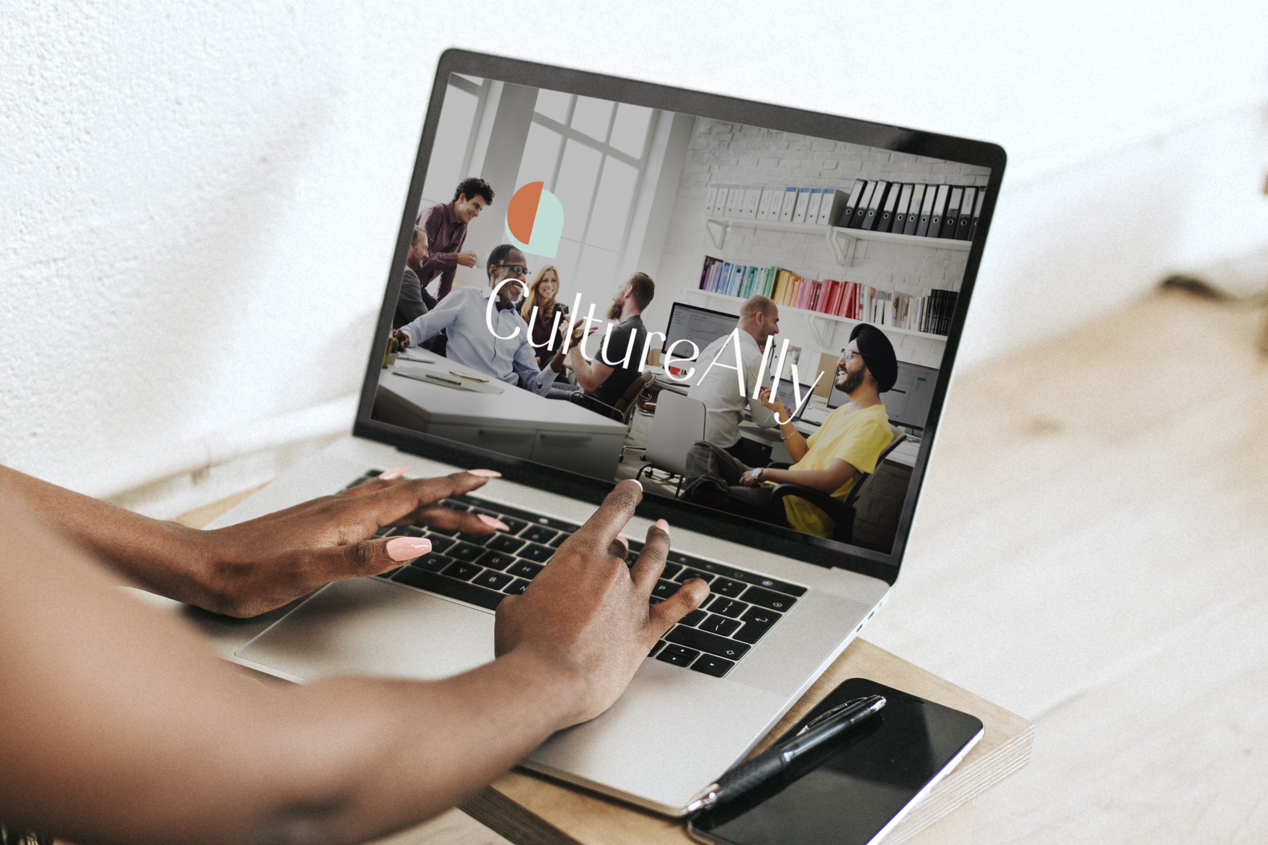 Person using a laptop showing a webpage with the text 'Culture Ally' and an image of a diverse group of people in an office setting.