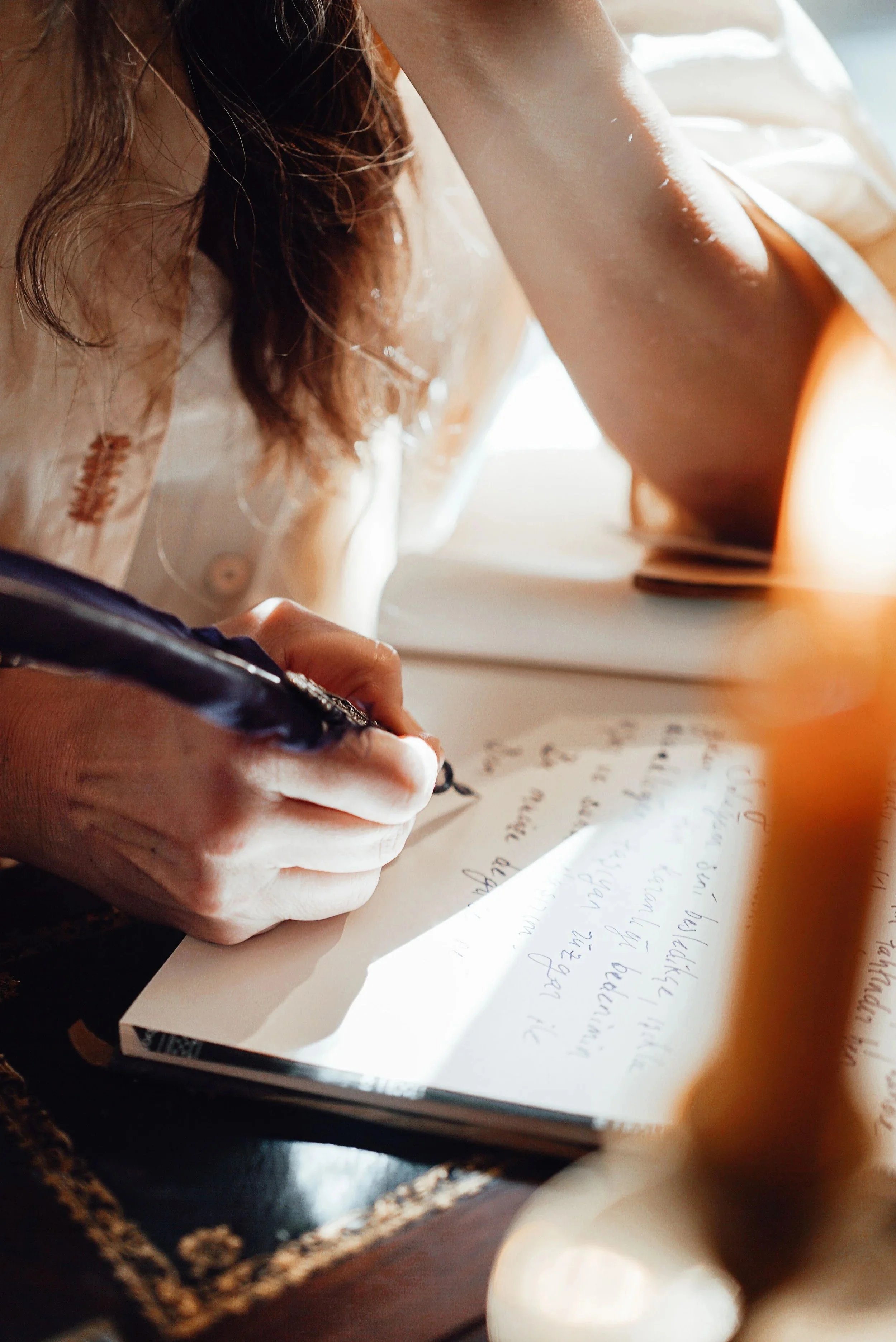 Close-up of a person writing on a handwritten letter with a black pen, with part of their face and arm visible in a natural light setting.