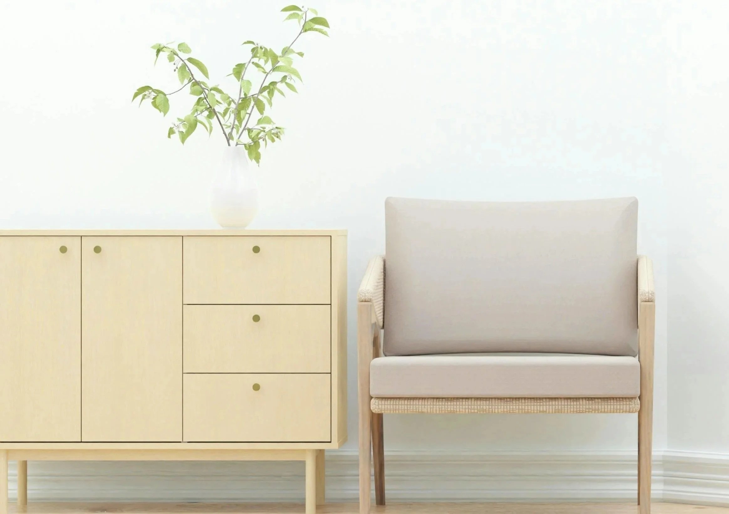 A yellow wooden cabinet with six drawers and round knobs, a white vase with green leafy branches, and a beige armchair with wooden legs against a plain white wall.