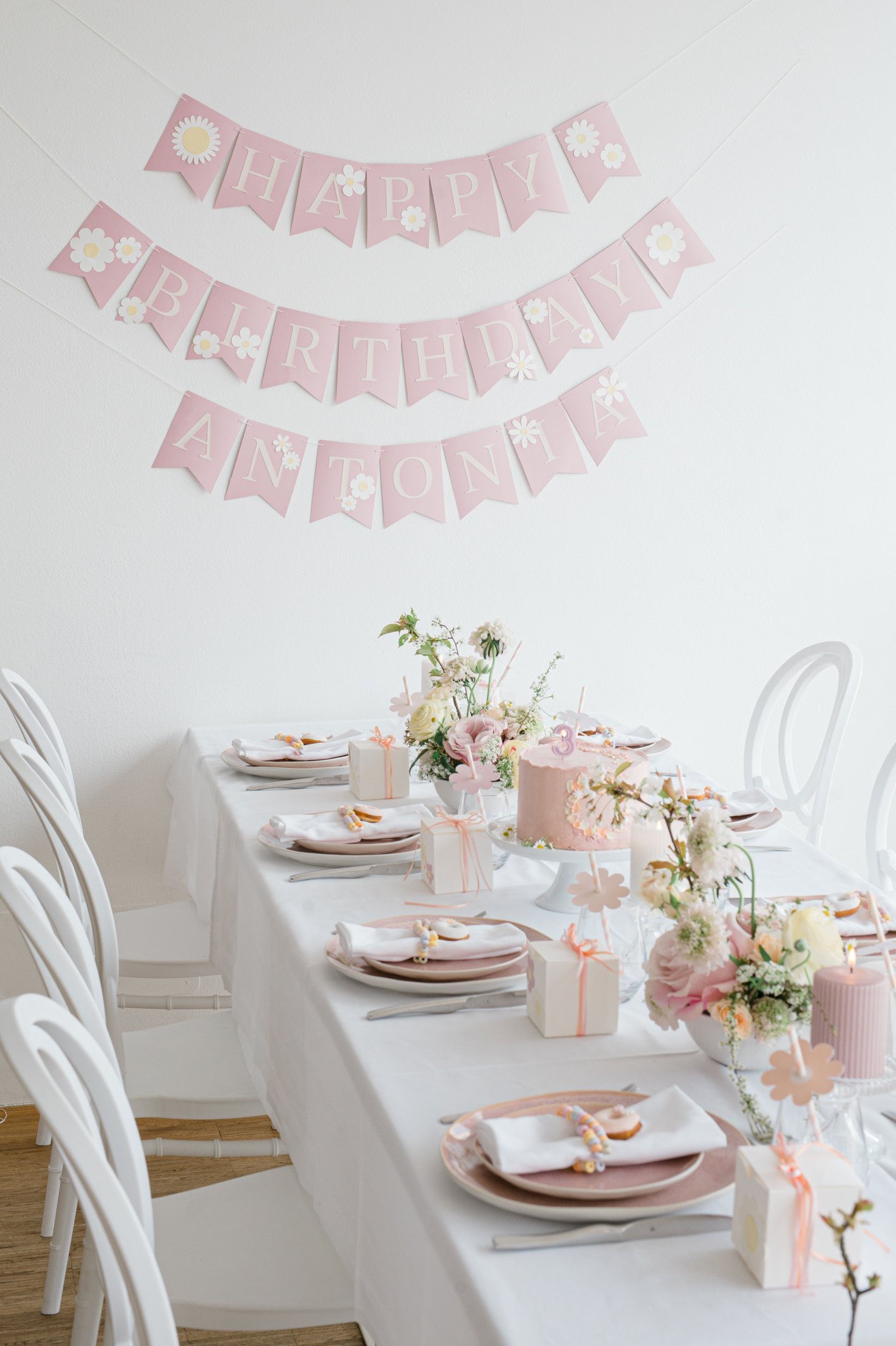 Ein festlich gedeckter Tisch in Weiß mit rosa Dekorationen, Blumen und Geschenken, Hintergrund mit Geburtstagsschmuck in Pastellfarben.