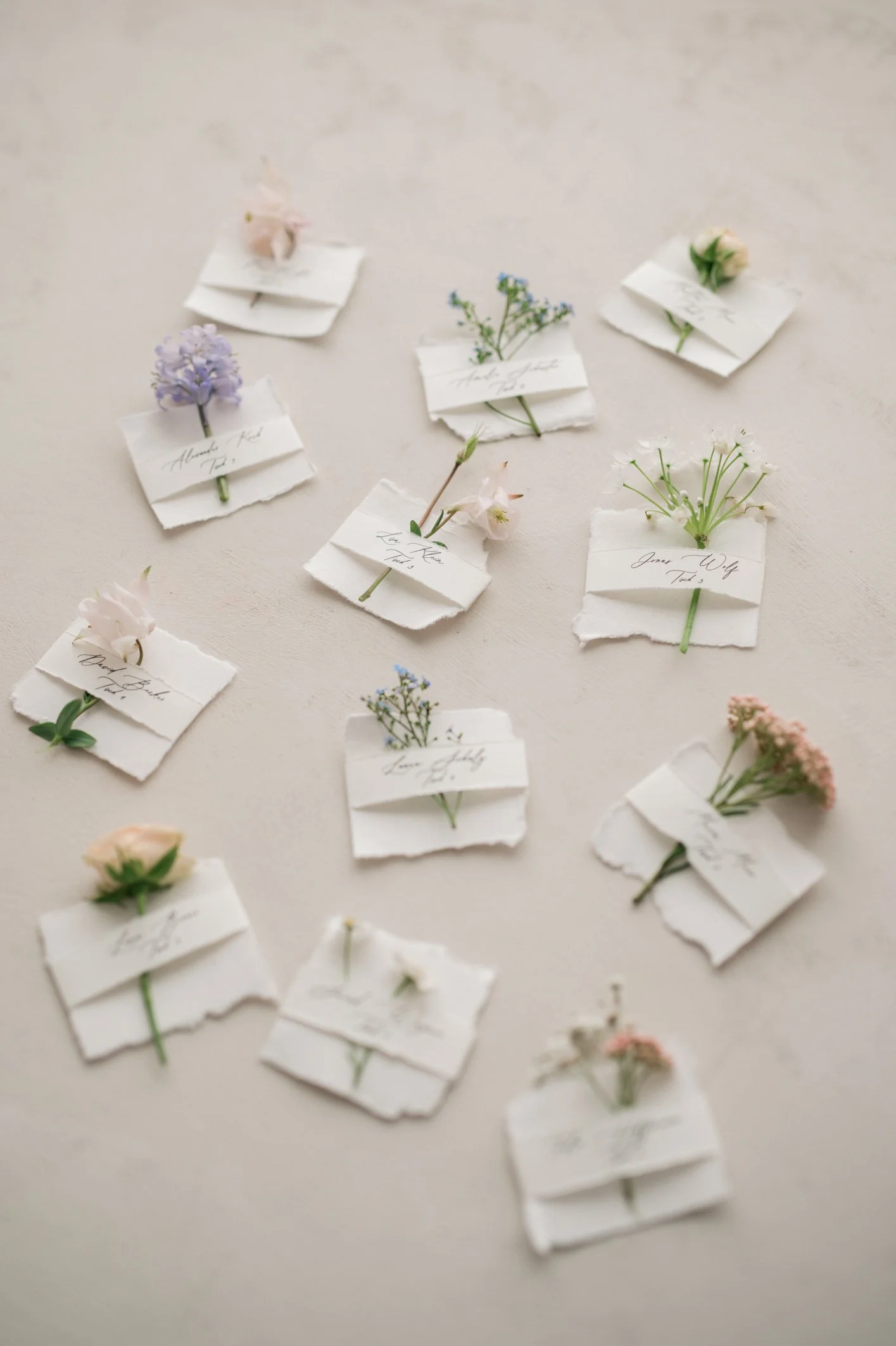 Verschiedene kleine Blumen, die an Papierstücken befestigt sind, liegen auf einer neutralen Oberfläche.