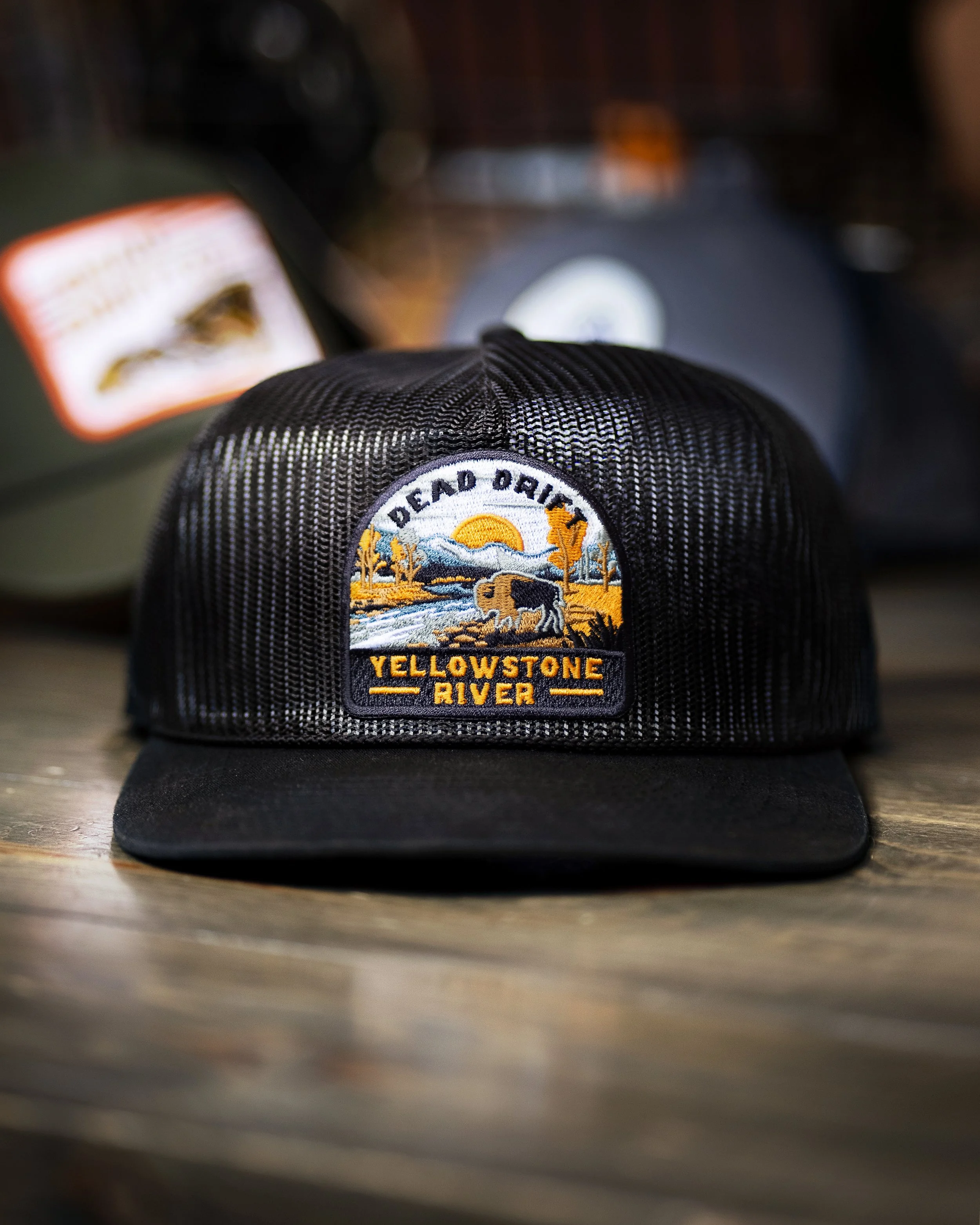 Close-up of a black baseball cap with a Yellowstone River patch, resting on a wooden surface.