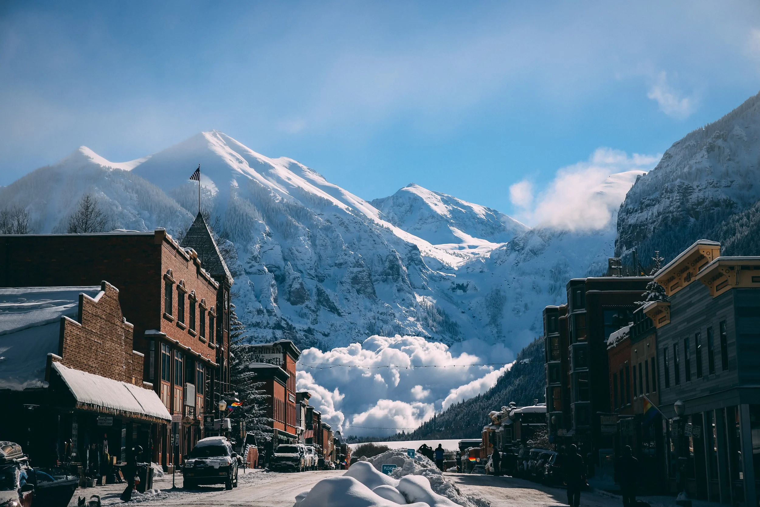 Snow-covered buildings on a busy street with mountains in the background