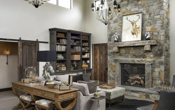 Living room with a stone fireplace, chandelier, bookshelf, gray couches, a sliding barn door, and decorative items.