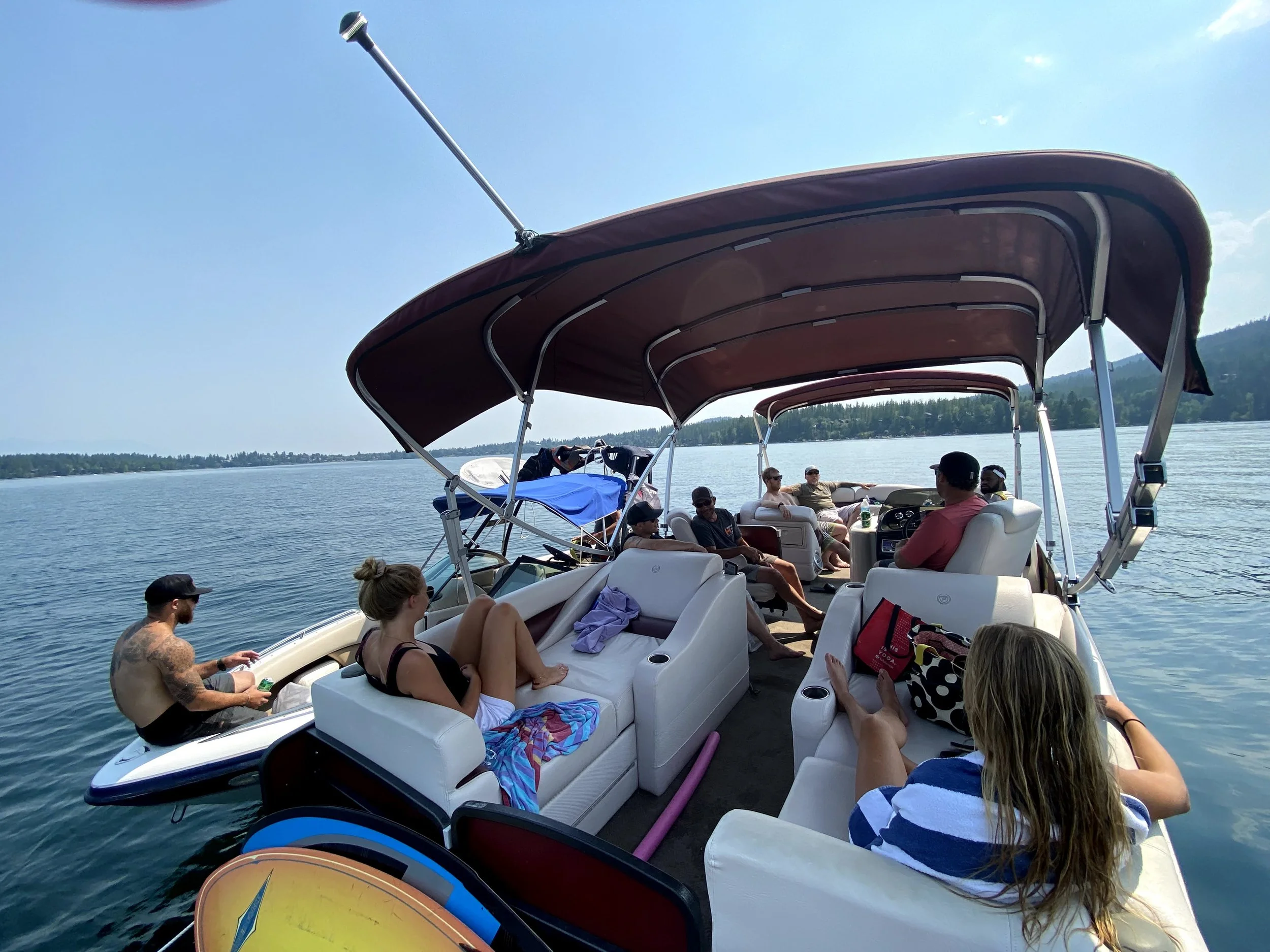 A group of people relaxing on a boat with a canopy on a lake under a blue sky.