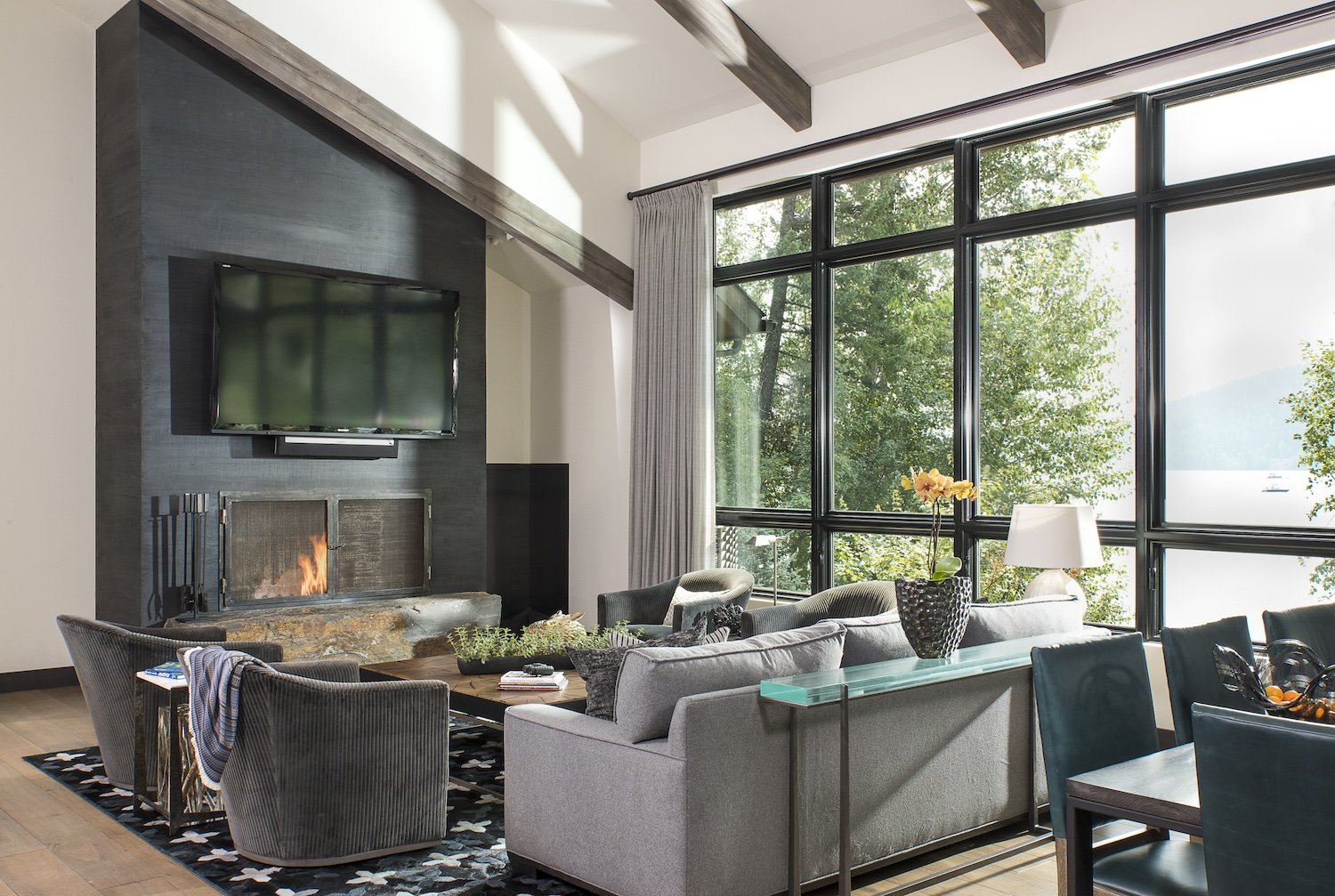 Living room with large windows, a gray sofa, armchairs, a fireplace, and a mounted television.