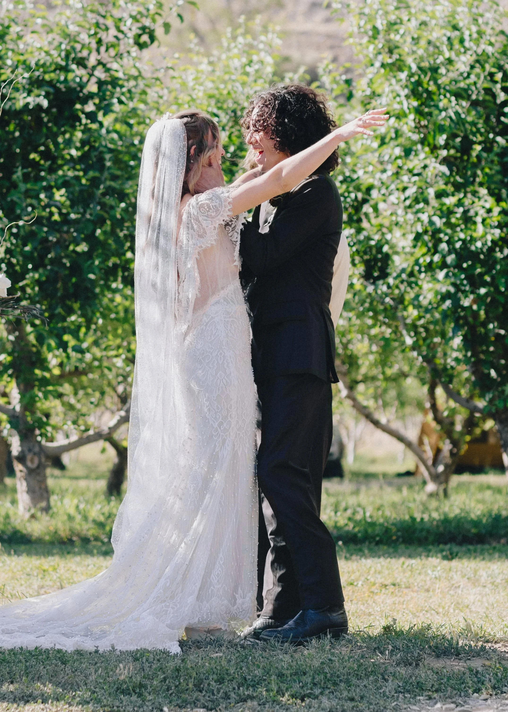 A wedding altar with a floral arch on a grassy lawn in front of a wooden fence.
