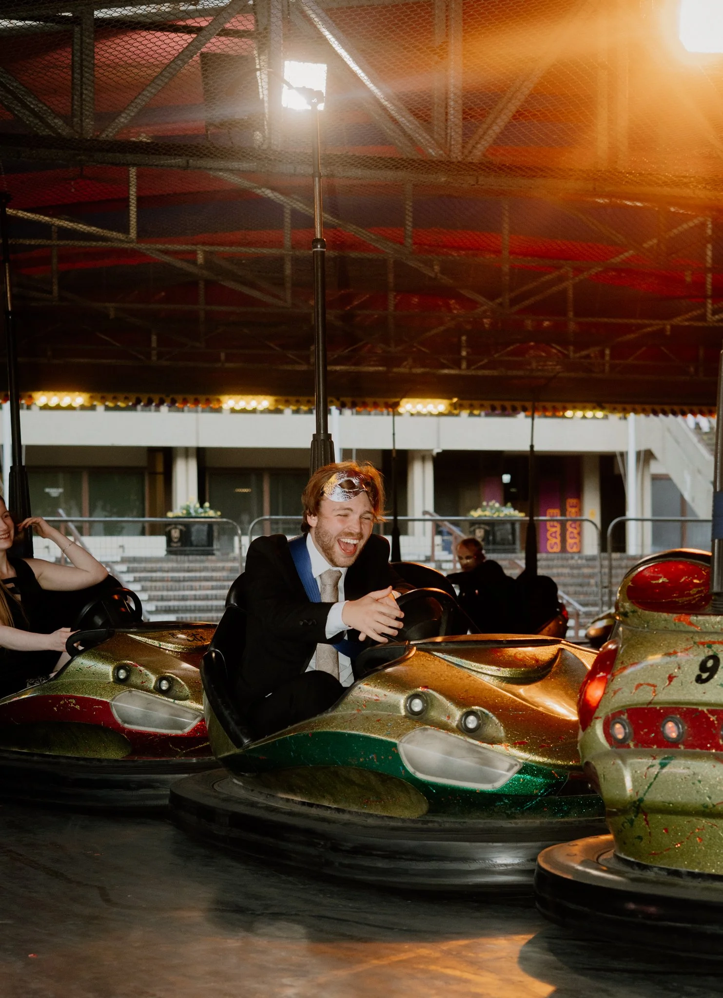 People enjoying bumper car rides at an amusement park, with a woman smiling and a man laughing, surrounded by colorful bumper cars under a canopy.