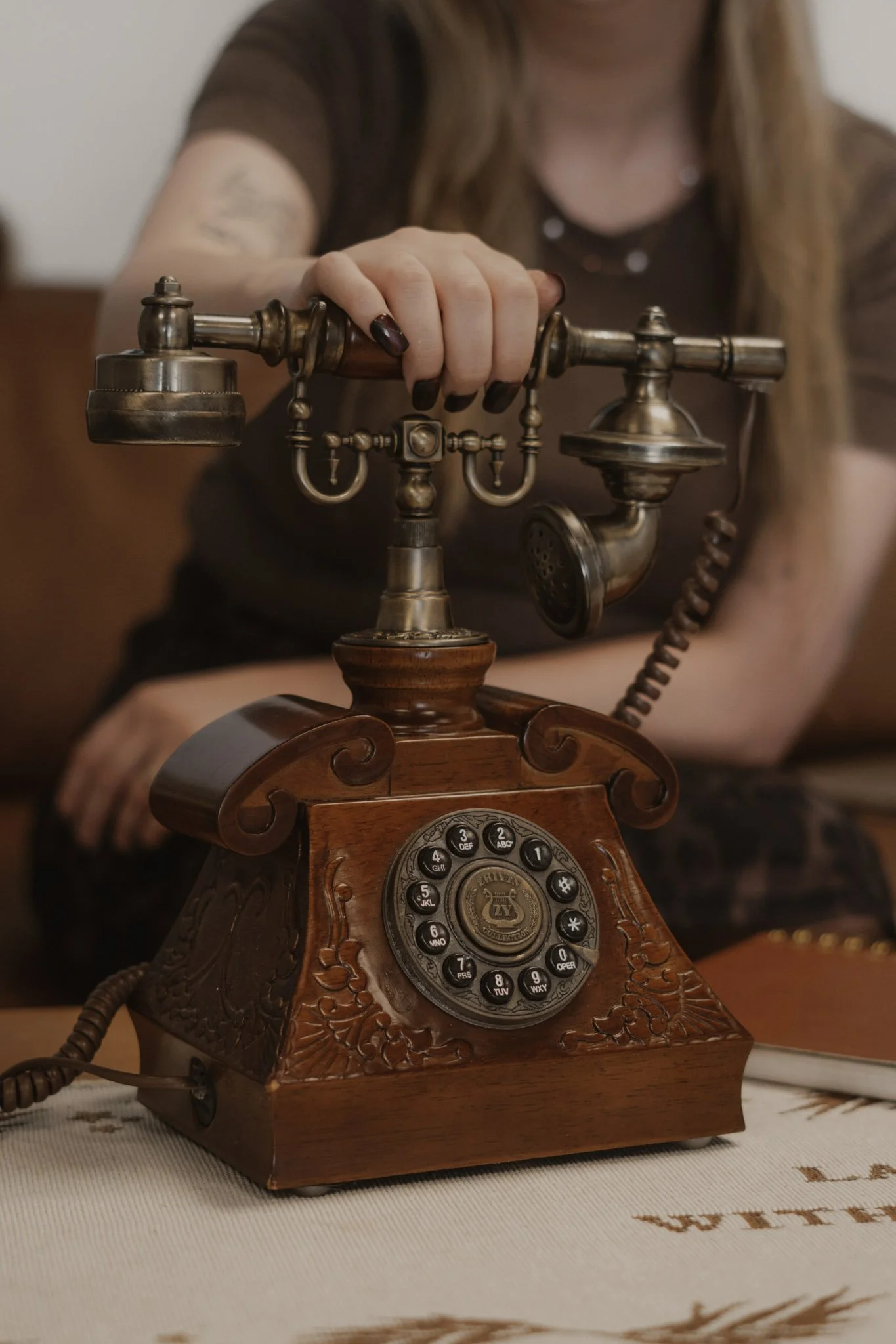 Vintage rotary telephone with a wooden base and ornate design, placed on a table with embroidered white cloth.