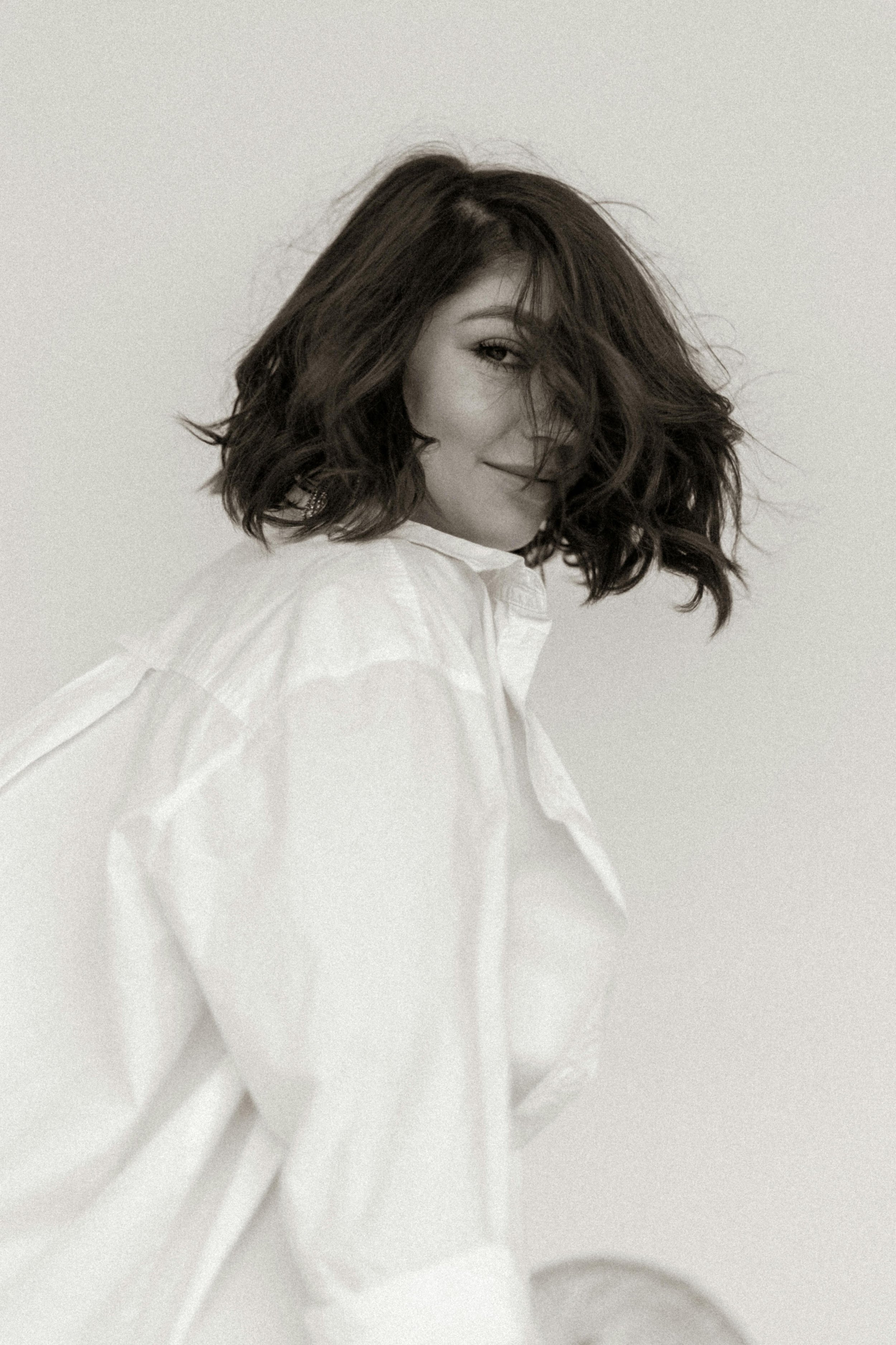 A woman with shoulder-length wavy hair, wearing a white shirt, smiling with her eyes slightly closed, against a plain background.