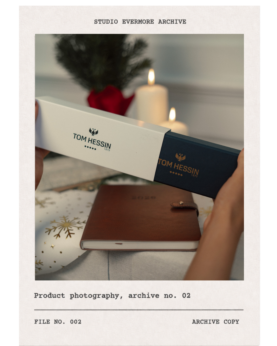 Person holding a Tom Hessin box with candles, a small Christmas tree, and a leather journal on a festive table.