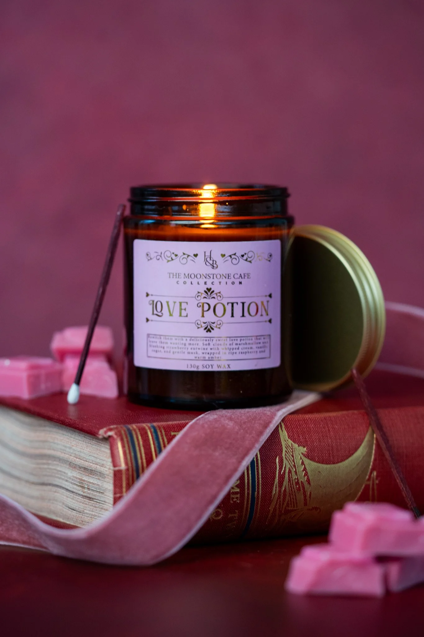 Styled product candle photography featuring a Love Potion candle with books, ribbon and pink wax melts.