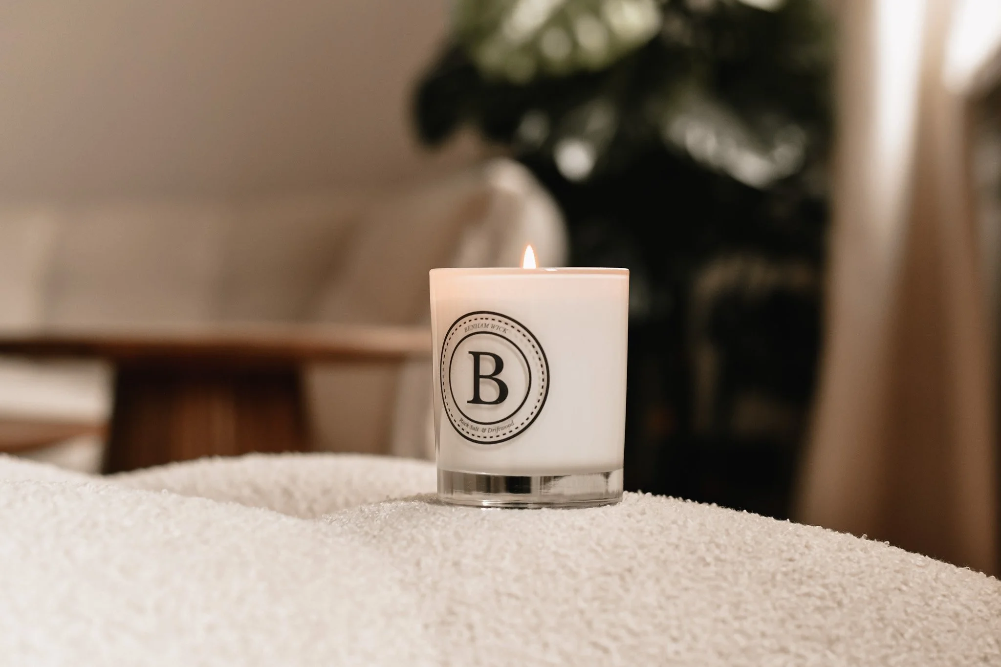 Styled product photography of a lit candle in a neutral lifestyle setting.