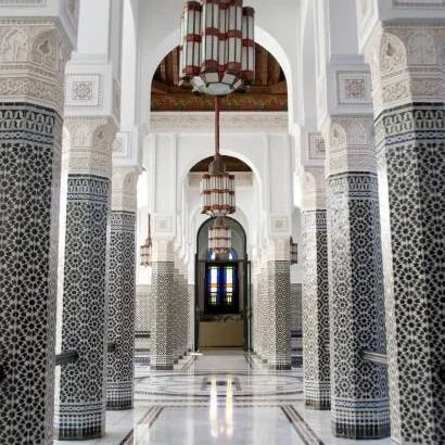 Interior of a building with ornate white walls, decorative columns with intricate tile work, and hanging lantern-style lights.