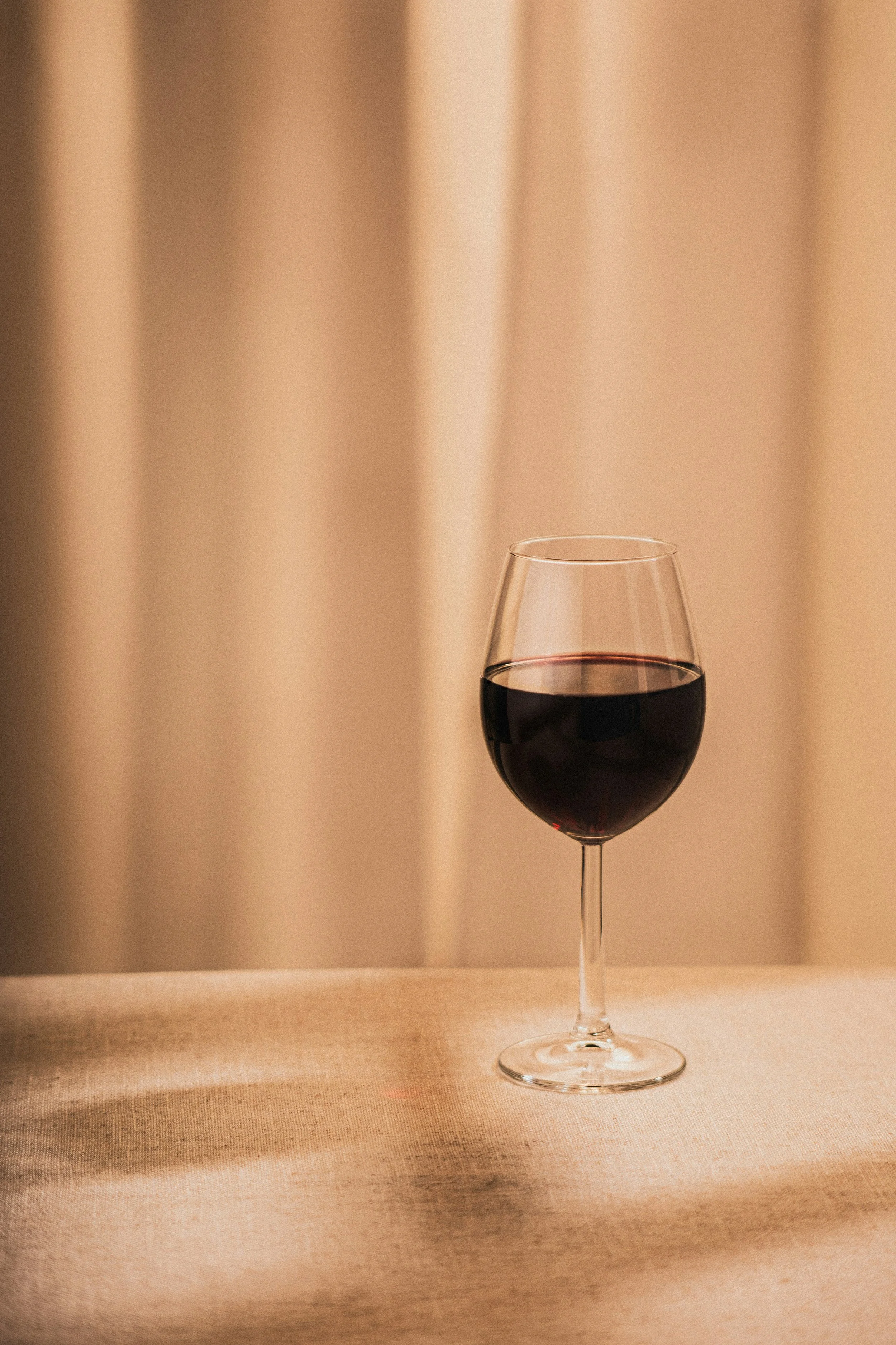 A glass of red wine on a neutral-colored table with a beige curtain background.
