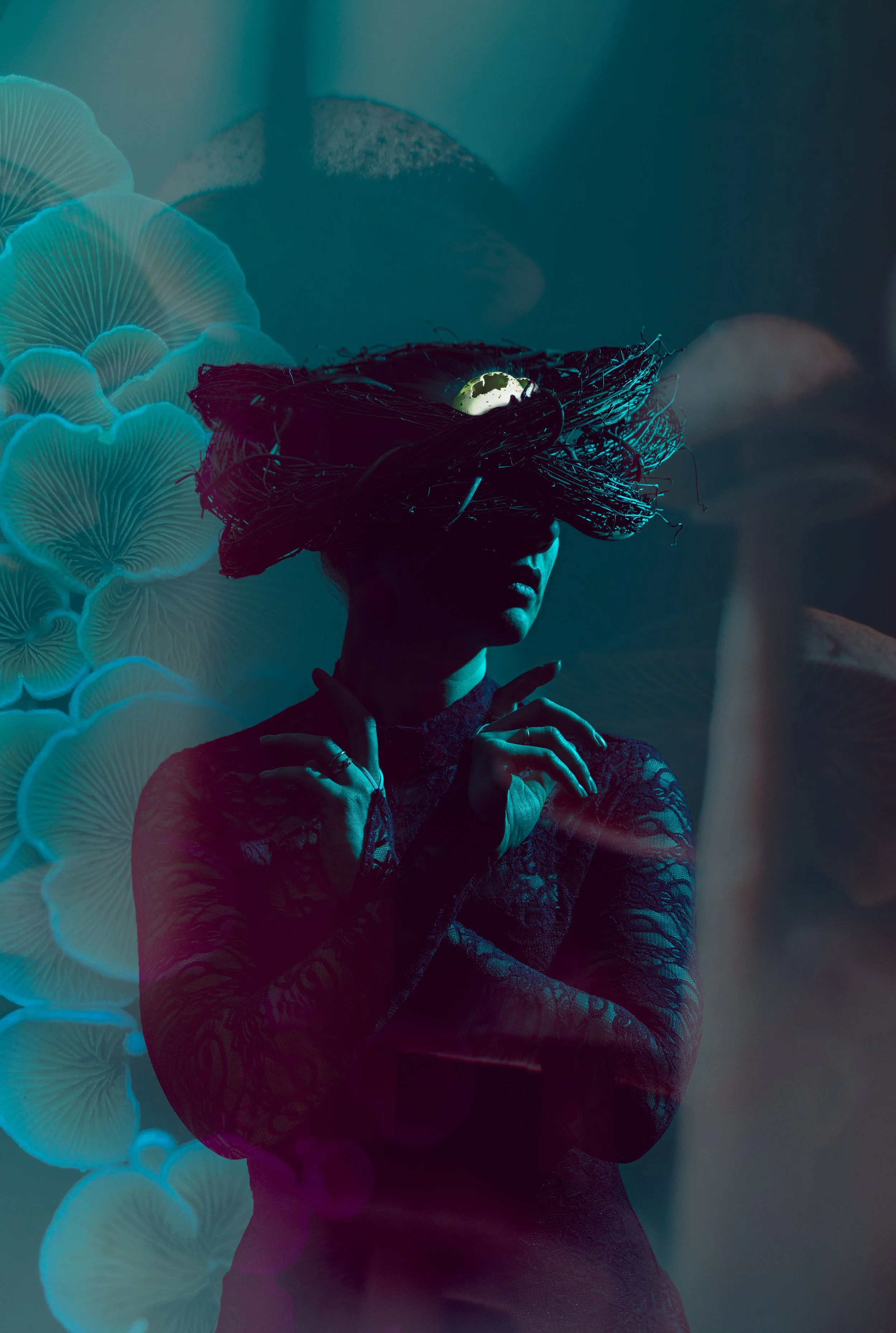 A woman wearing a lace dress and a dramatic headpiece made of dark twigs with an earth-shaped ornament on top, standing in front of a backdrop of white, glowing mushroom-like shapes.
