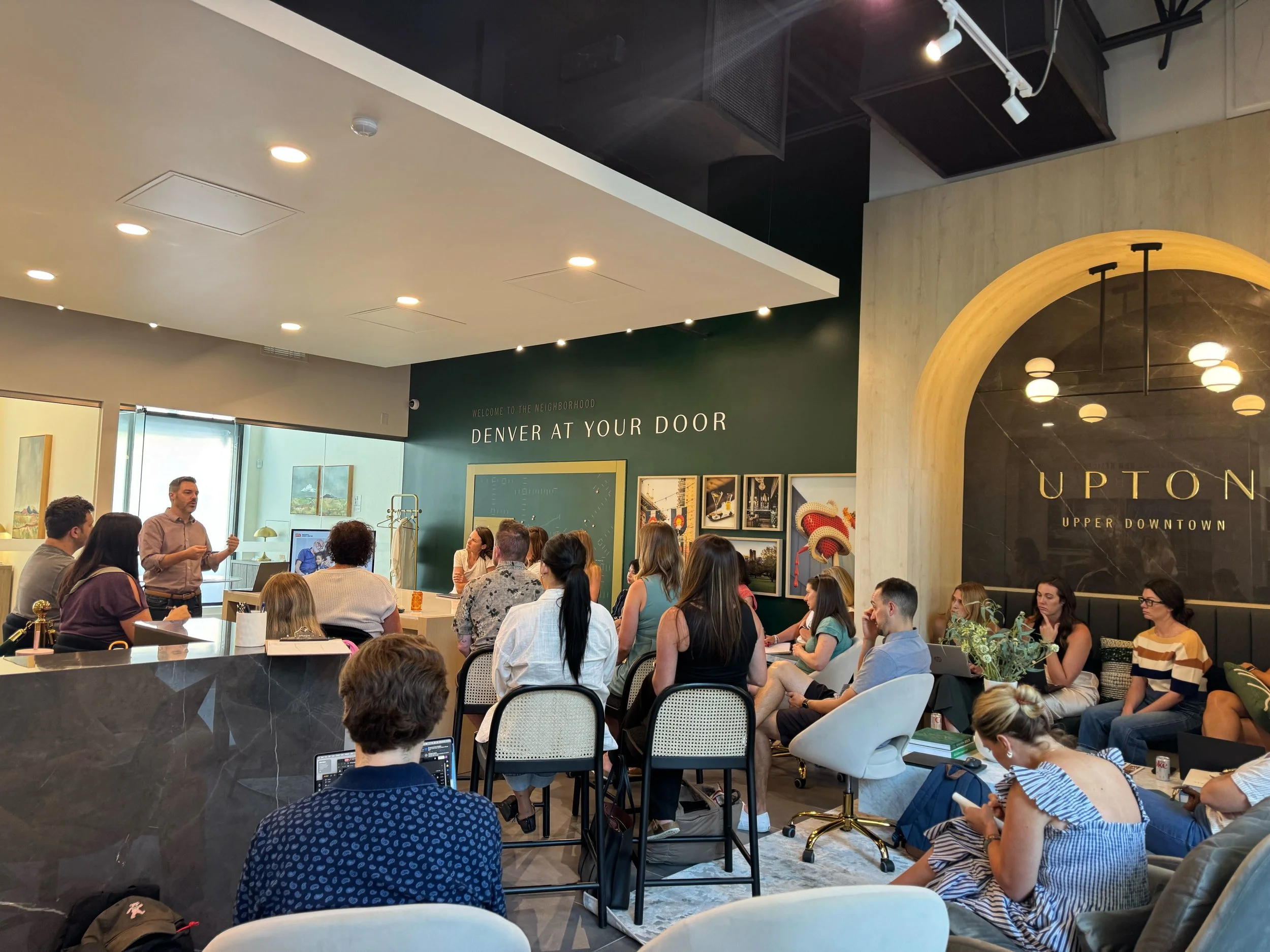 A group of people attending a presentation in a modern, stylish indoor space with artwork on the walls and comfortable seating.
