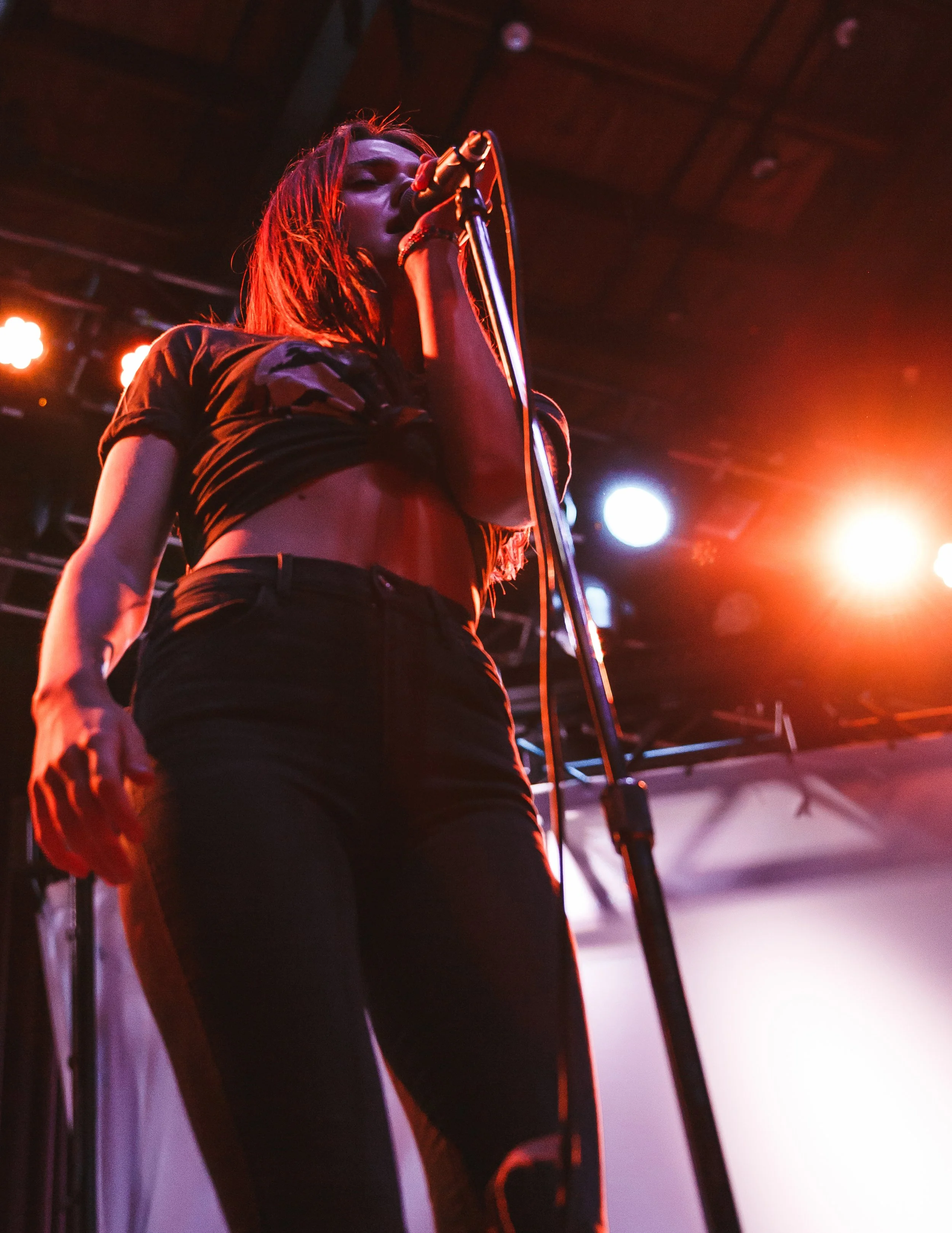 A woman with long hair singing into a microphone on stage, lit by colorful stage lights.