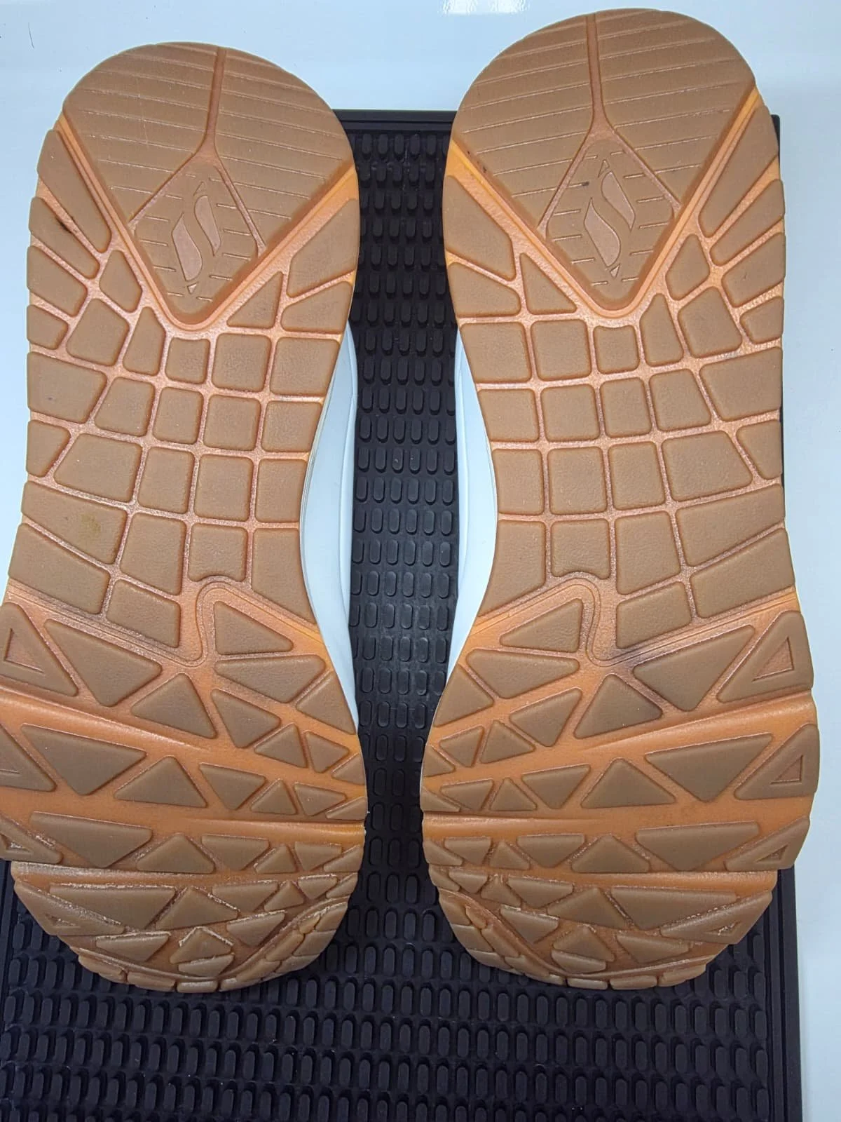 Close-up of the sole of a running shoe, showing a patterned tread in tan, black, and white colors.