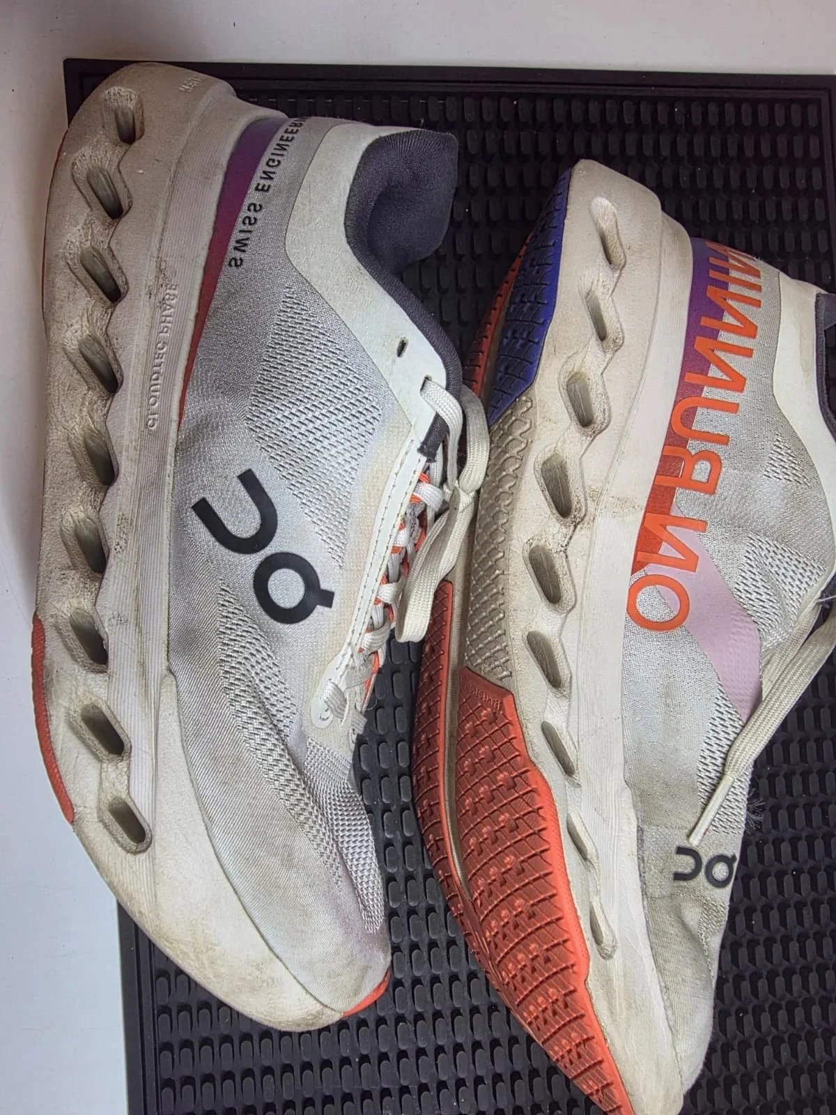 Pair of off-white athletic shoes with multicolored accents and the words "OWN THE RUN" on the side, placed on a black textured surface.