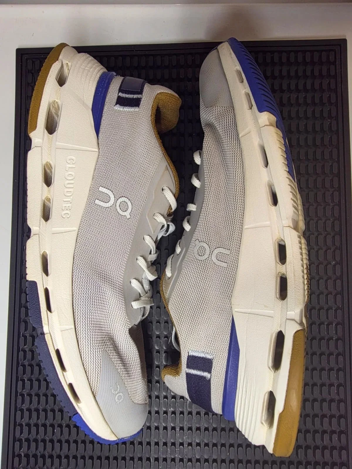 Pair of athletic sneakers with beige, blue, and white details, placed on a textured black surface.
