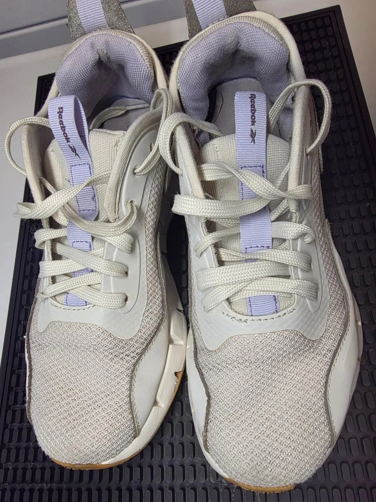 A pair of white Reebok sneakers placed on a black rubber surface.
