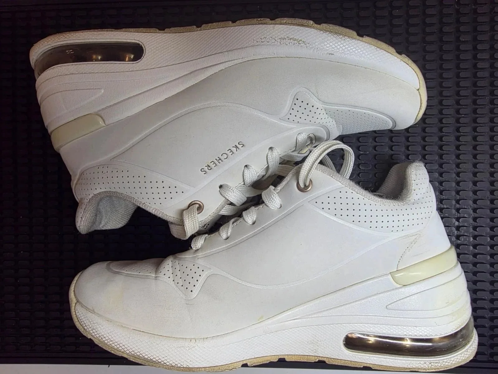 A pair of white Skechers sneakers with perforated details, placed on a black textured surface.