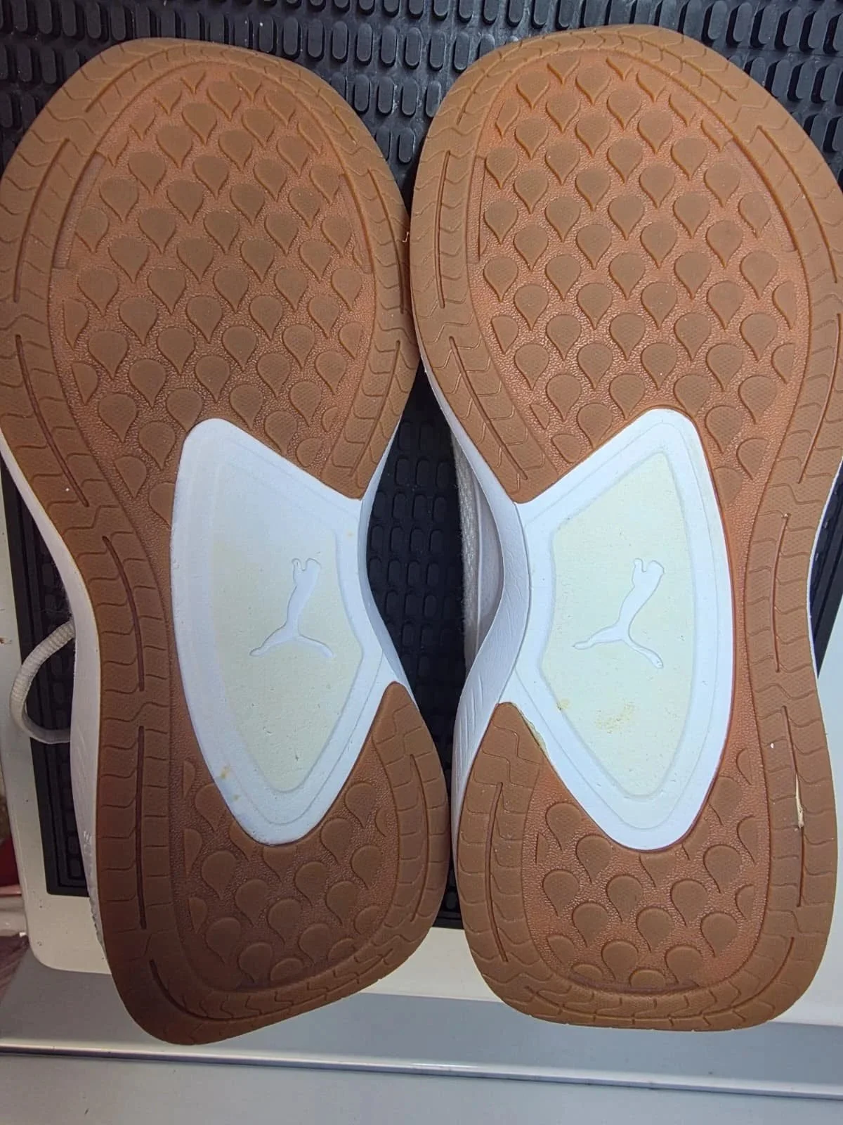 The image shows the soles of two Puma athletic shoes placed side by side, viewed from the bottom, with a brown and white color scheme and textured patterns.