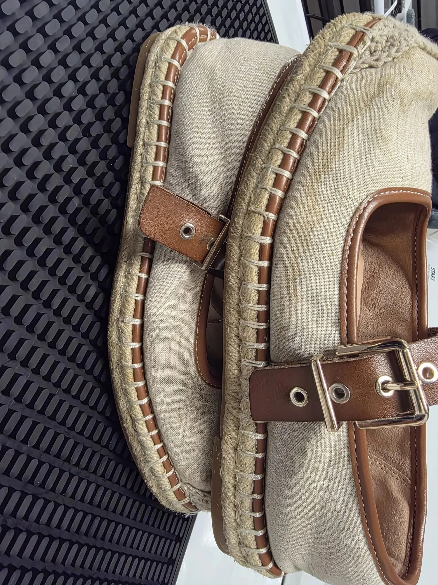 Close-up of a beige canvas bag with brown leather trim and a buckle, resting on a black textured surface.