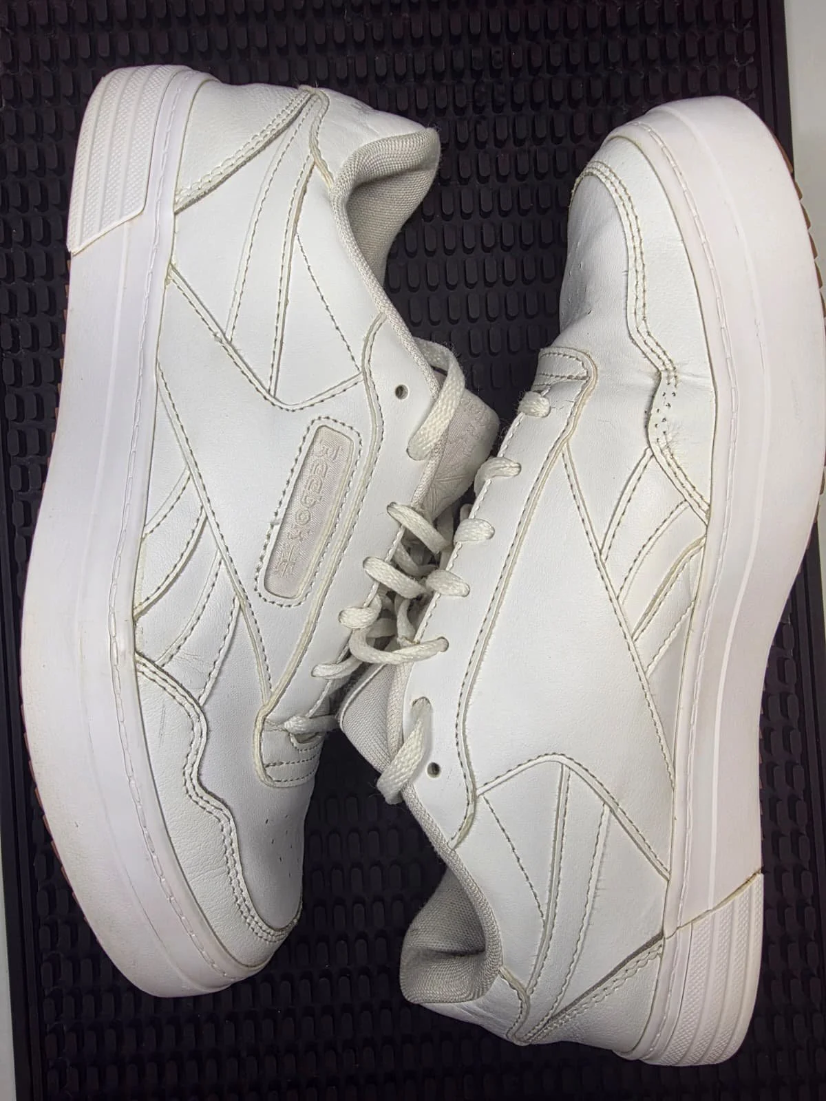 White sneakers placed on a black textured surface.