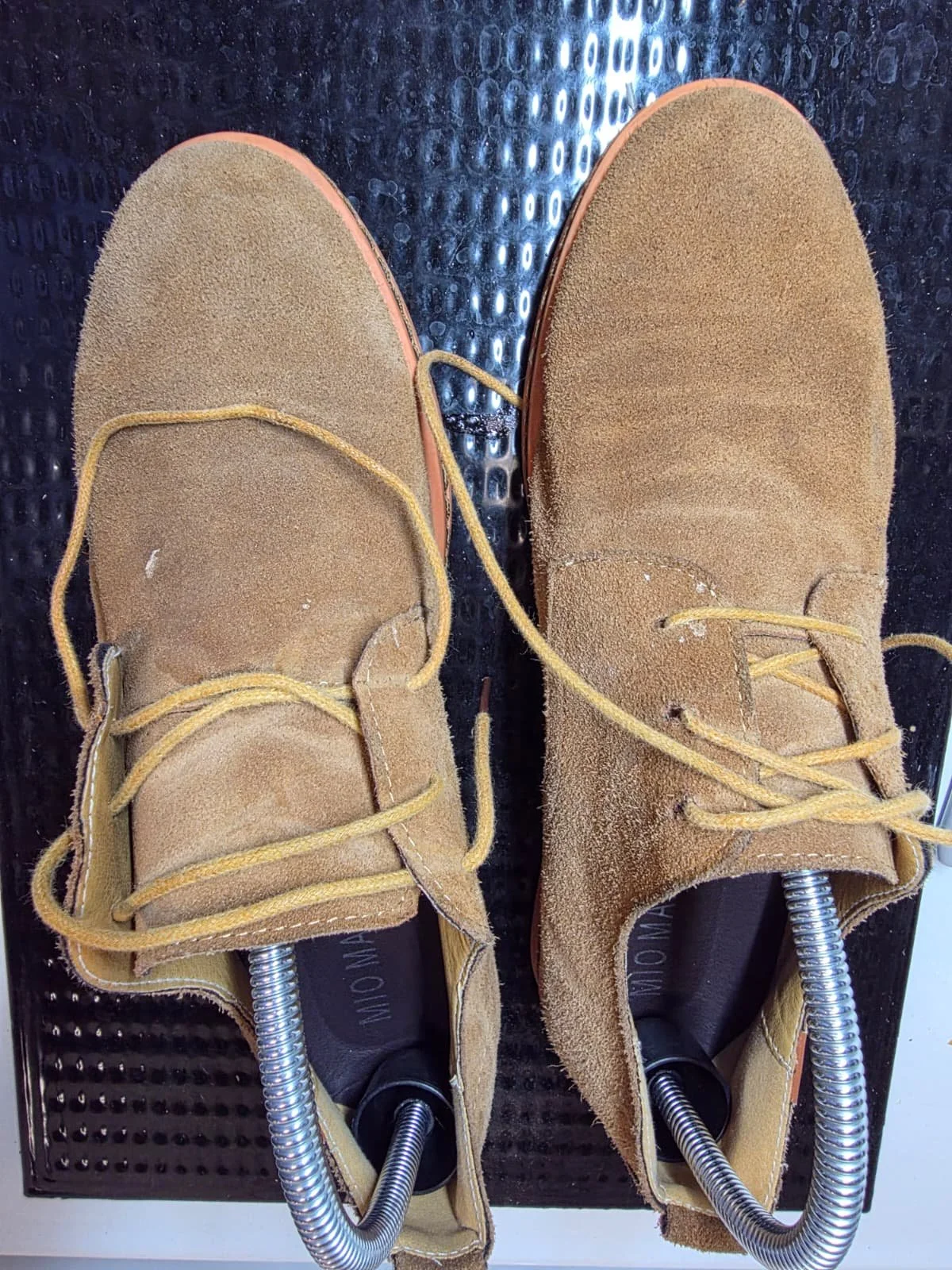 Pair of yellow suede shoes on a shoe testing machine with metal springs.