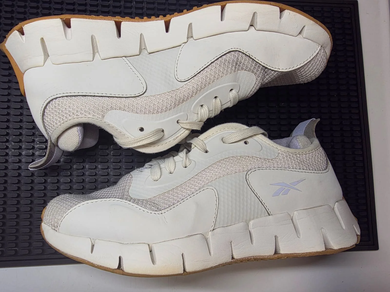A pair of white athletic shoes with silver and grey accents on a black textured surface.