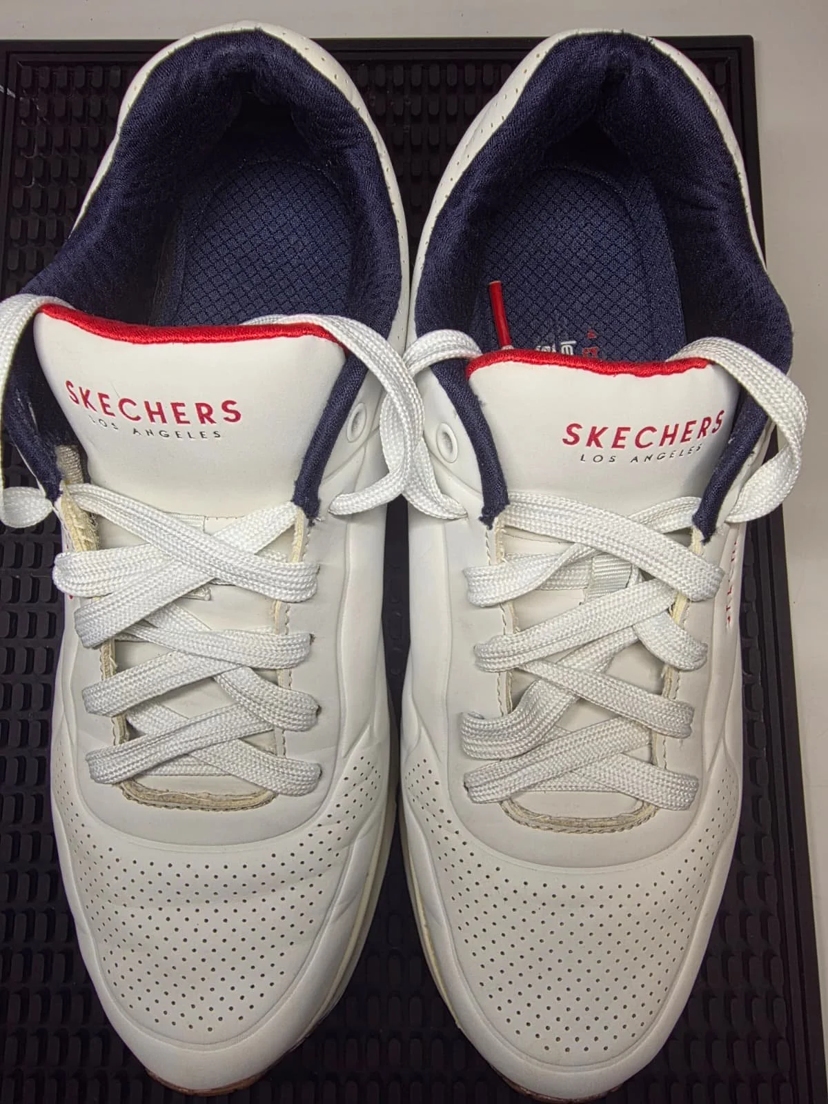Pair of white Skechers sneakers with navy blue inner lining and red accents, placed side by side.