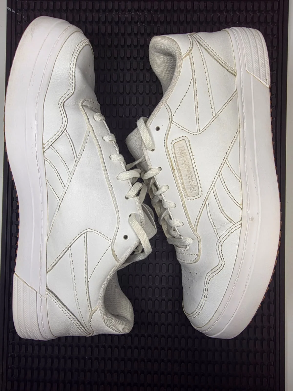 Pair of white Reebok athletic sneakers placed on a black textured surface.