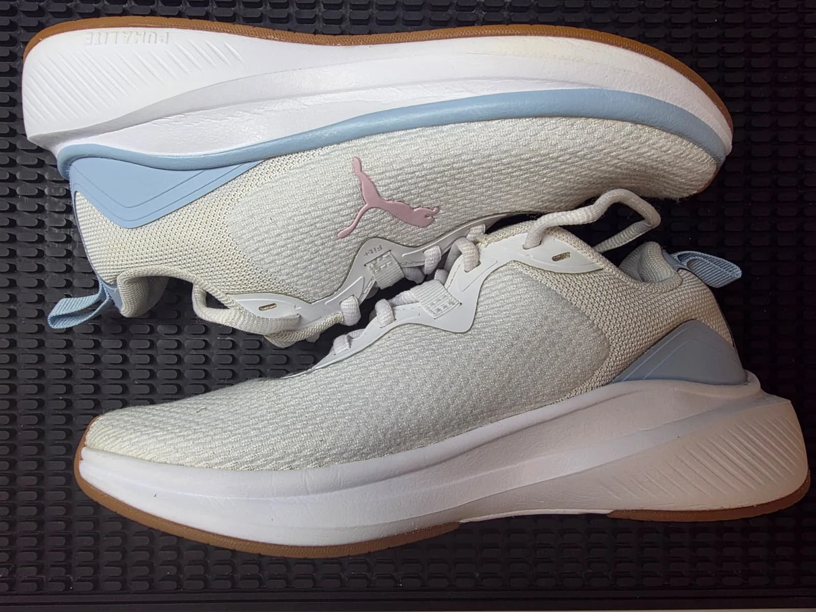A pair of Puma running shoes in white, beige, light blue, and gum sole color, placed on a black textured surface.