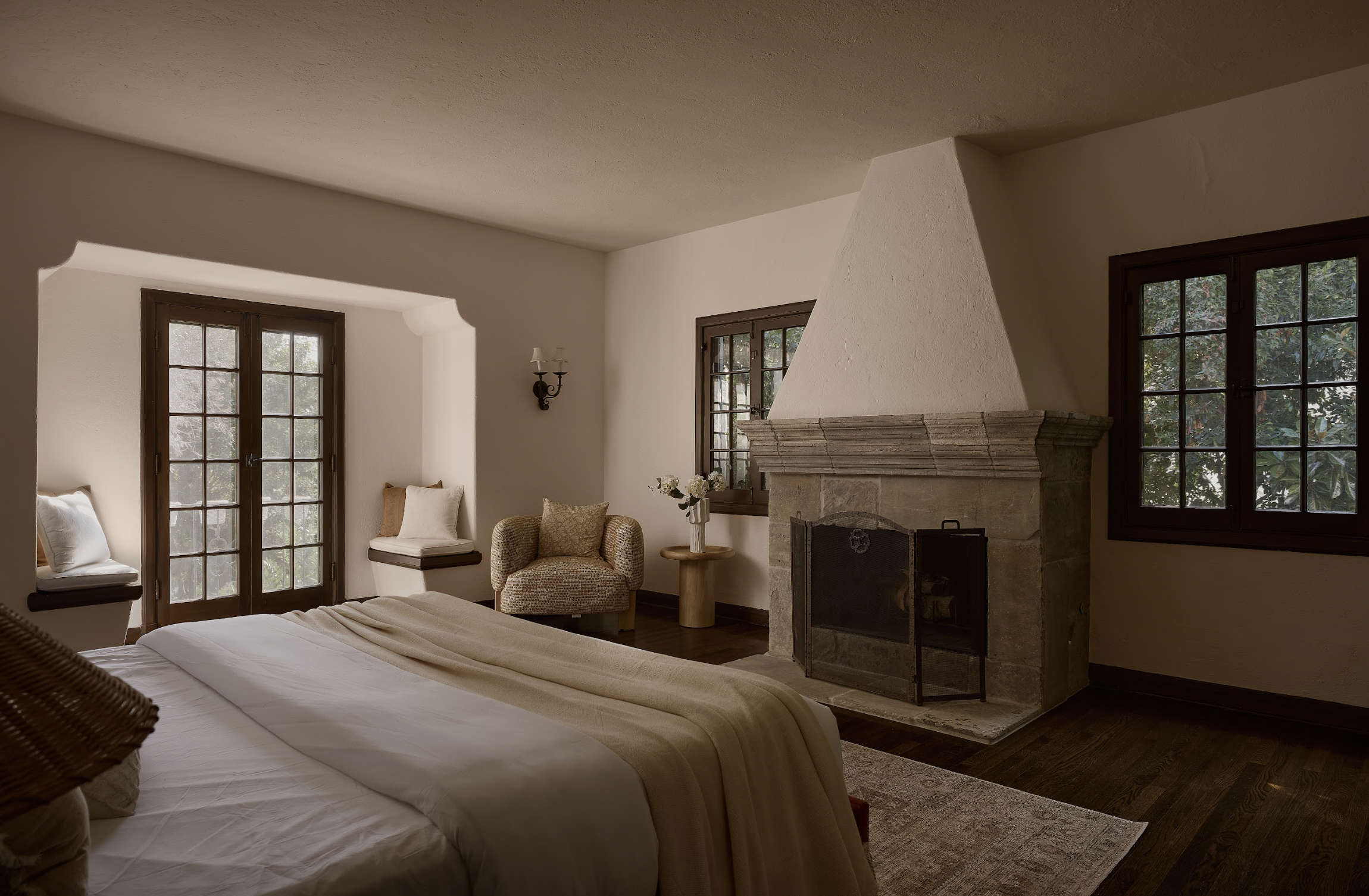 Luxury primary bedroom in a historic Hancock Park residence, staged by Francesca Grace, featuring a stone fireplace, custom millwork, and layered neutral furnishings.