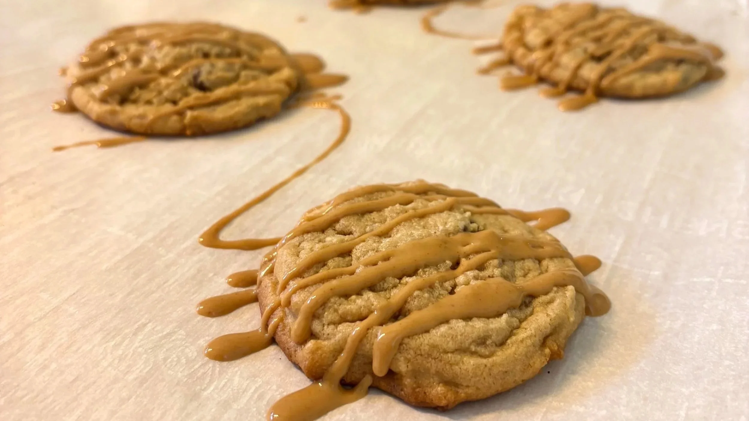 Close-up of peanut butter cup cookies drizzled with peanut butter sauce on a parchment paper-lined surface.