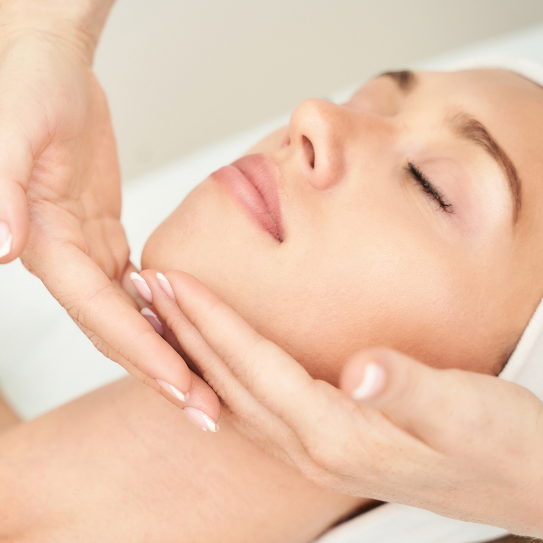 Close-up of a woman with closed eyes receiving a facial massage with her hand gently touching her cheek.