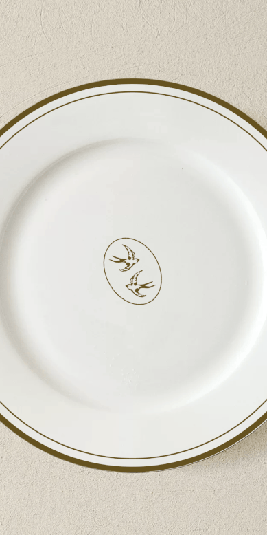 Assiette blanche avec un dessin de deux oiseaux stylisés au centre, entourée d'un contour or.