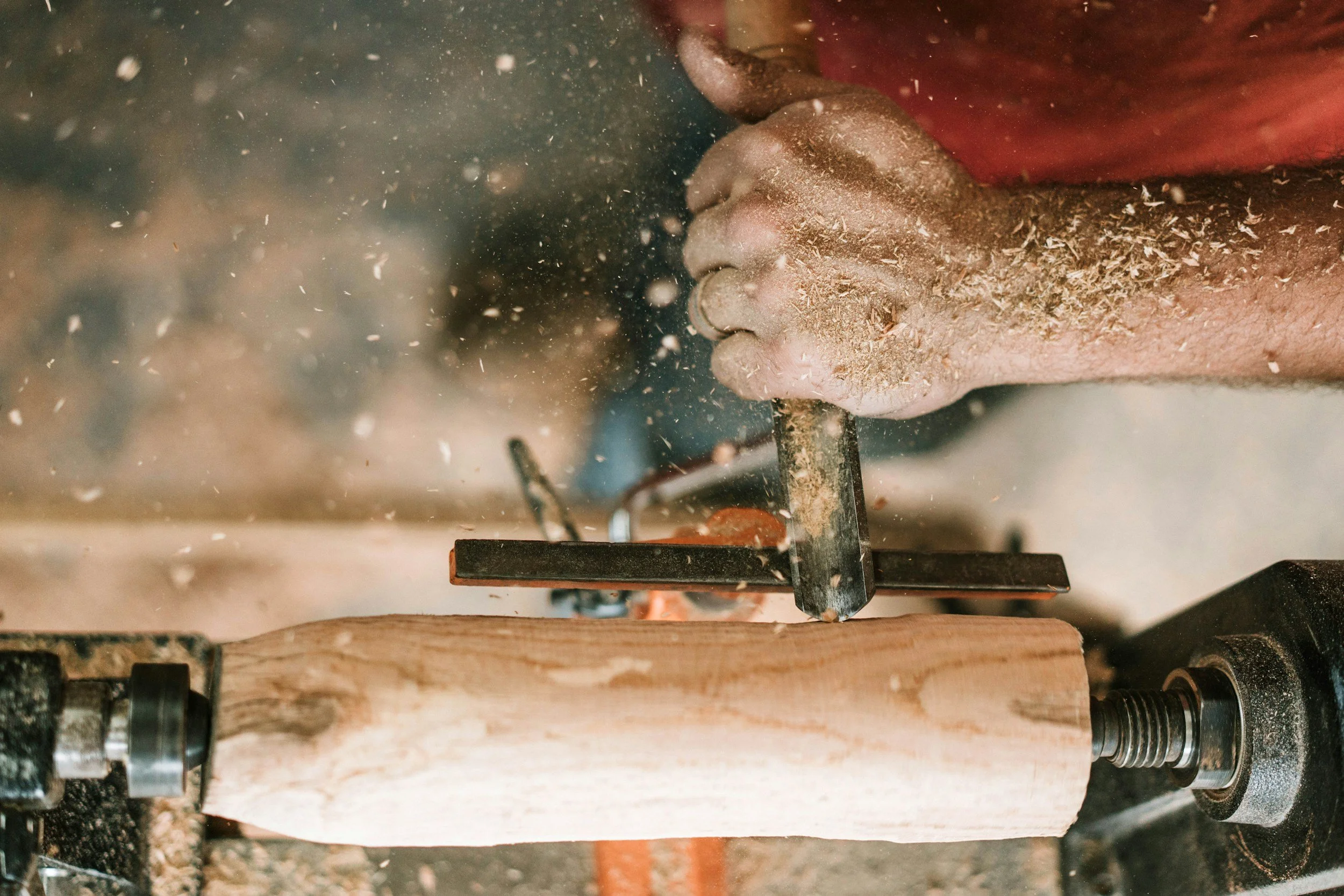 Close-up of a hand holding a small axe or hatchet, chopping a piece of wood with sawdust flying around.