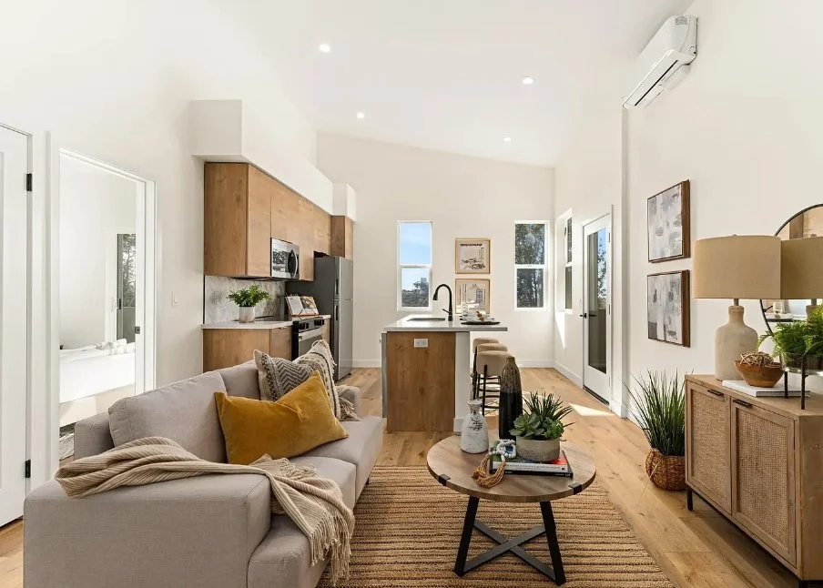 Open-concept living room and kitchen with natural light, wooden furniture, and modern decor