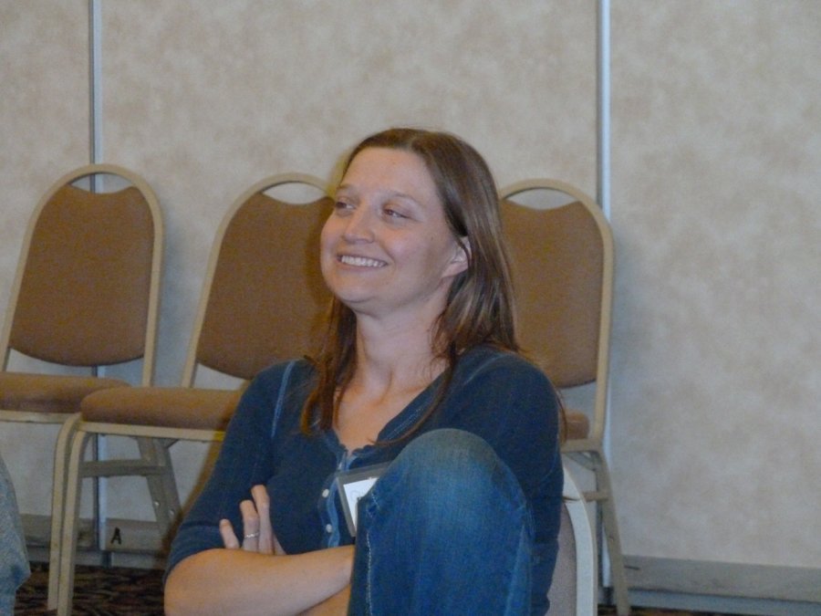Woman sitting on the floor with her arms crossed, smiling, in front of a row of chairs in a conference room.