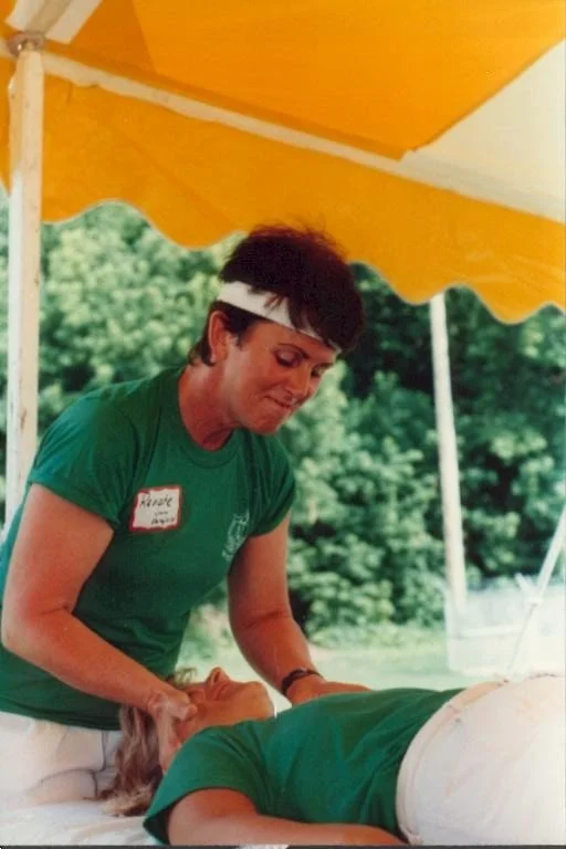 A woman giving a massage outdoors under a yellow canopy, with green trees in the background.