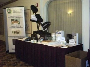 A table with various promotional items, flyers, and brochures in a room with patterned carpet and a mirror on the wall.