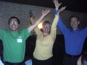 Three people celebrating indoors with their hands raised and smiling.